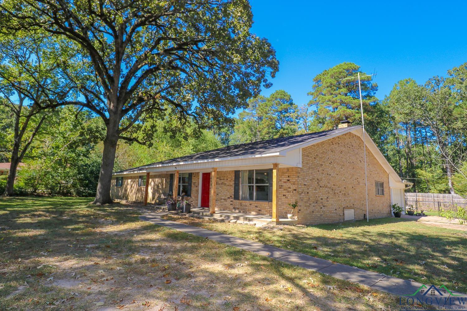 Image 1: Single story home featuring brick siding, a porch, a chimney, and view of wooded area, Front Of Structure