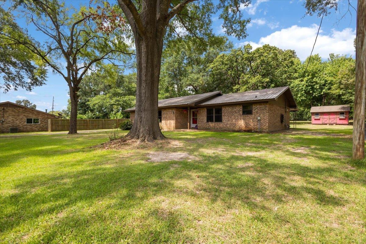 Image 1: Expansive green lawn with mature trees and a brick-sided residence, Front Of Structure
