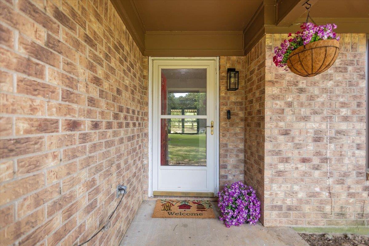 Image 2: Brick exterior with a covered entryway, featuring a white storm door with a brass handle, an outdoor wall sconce, and a concrete porch, Entry