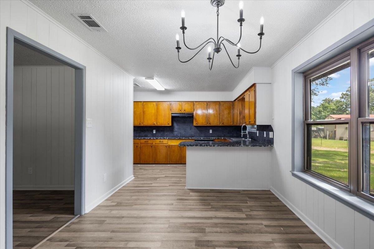 Image 3: Spacious dining area featuring wood-finish flooring, a contemporary chandelier, and paneling accents, Kitchen