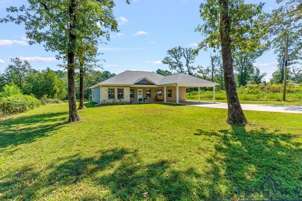 Image 1: View of front facade with an attached carport, concrete driveway, a front yard, covered porch, and stone siding, Front Of Structure
