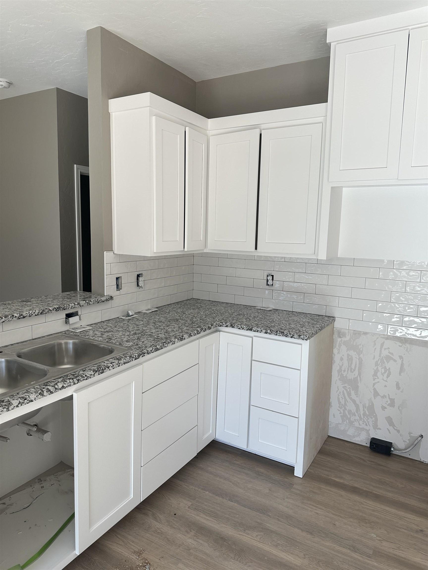Image 2: Kitchen with white cabinetry, dark wood finished floors, tasteful backsplash, and dark stone counters, Kitchen