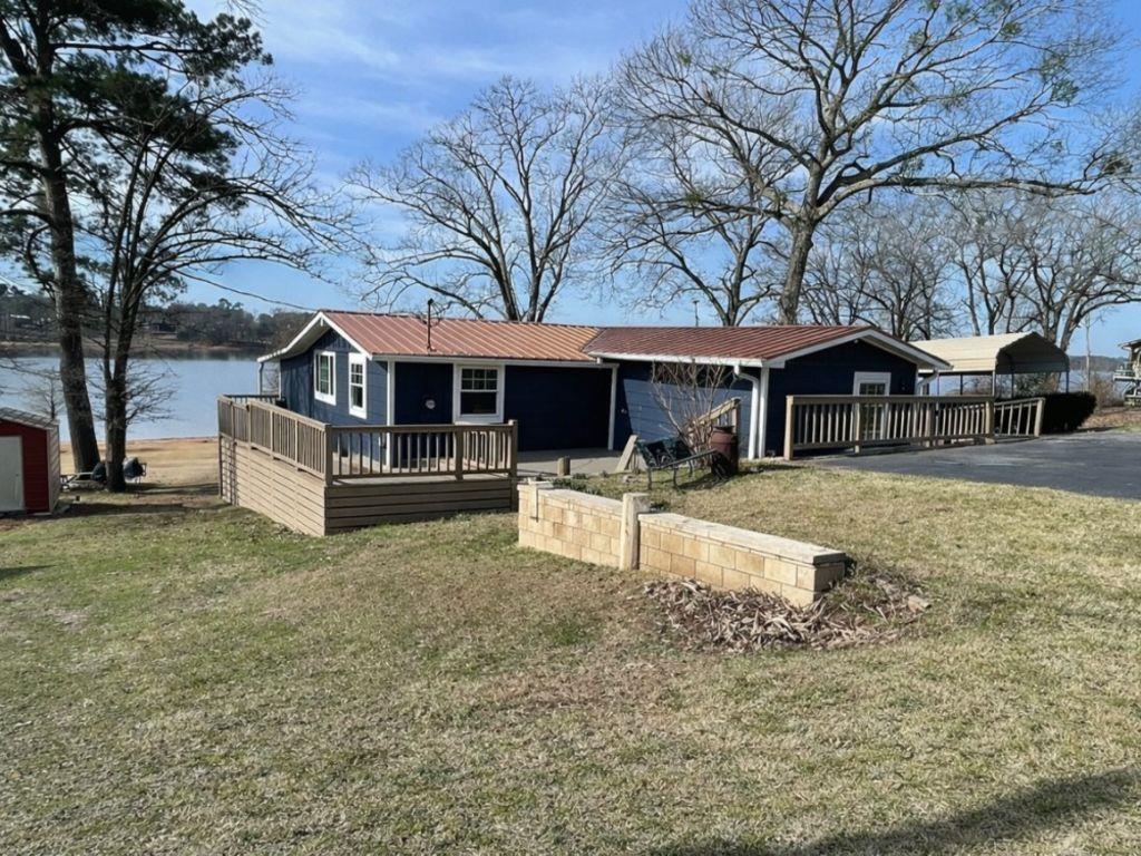 Image 1: View of front of home featuring a deck with water view, a front lawn, a metal roof, and asphalt driveway, Front Of Structure