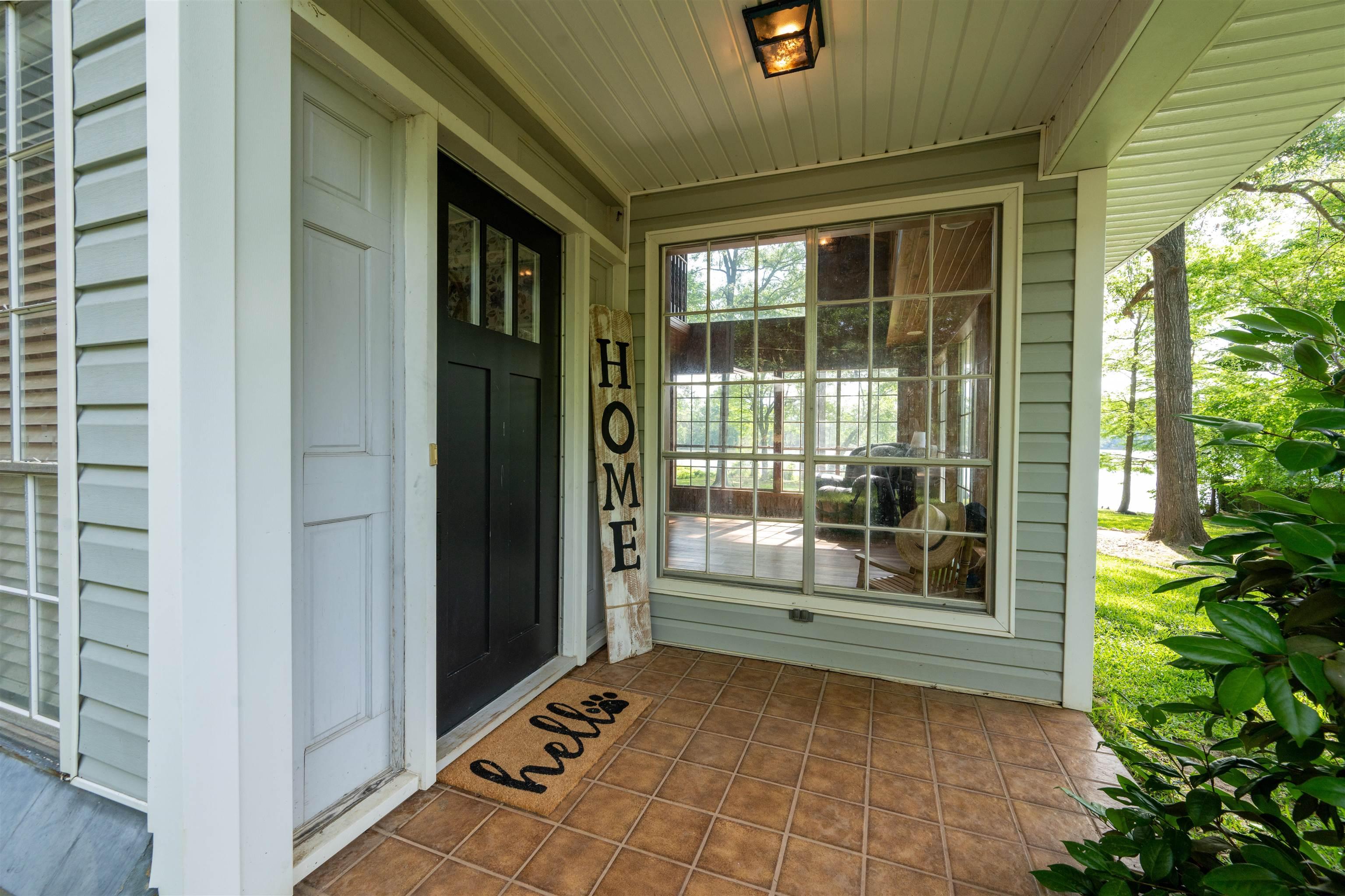 Image 1: Covered front porch featuring a dark paneled entry door with transom windows, light blue siding, and durable tile flooring, Entry