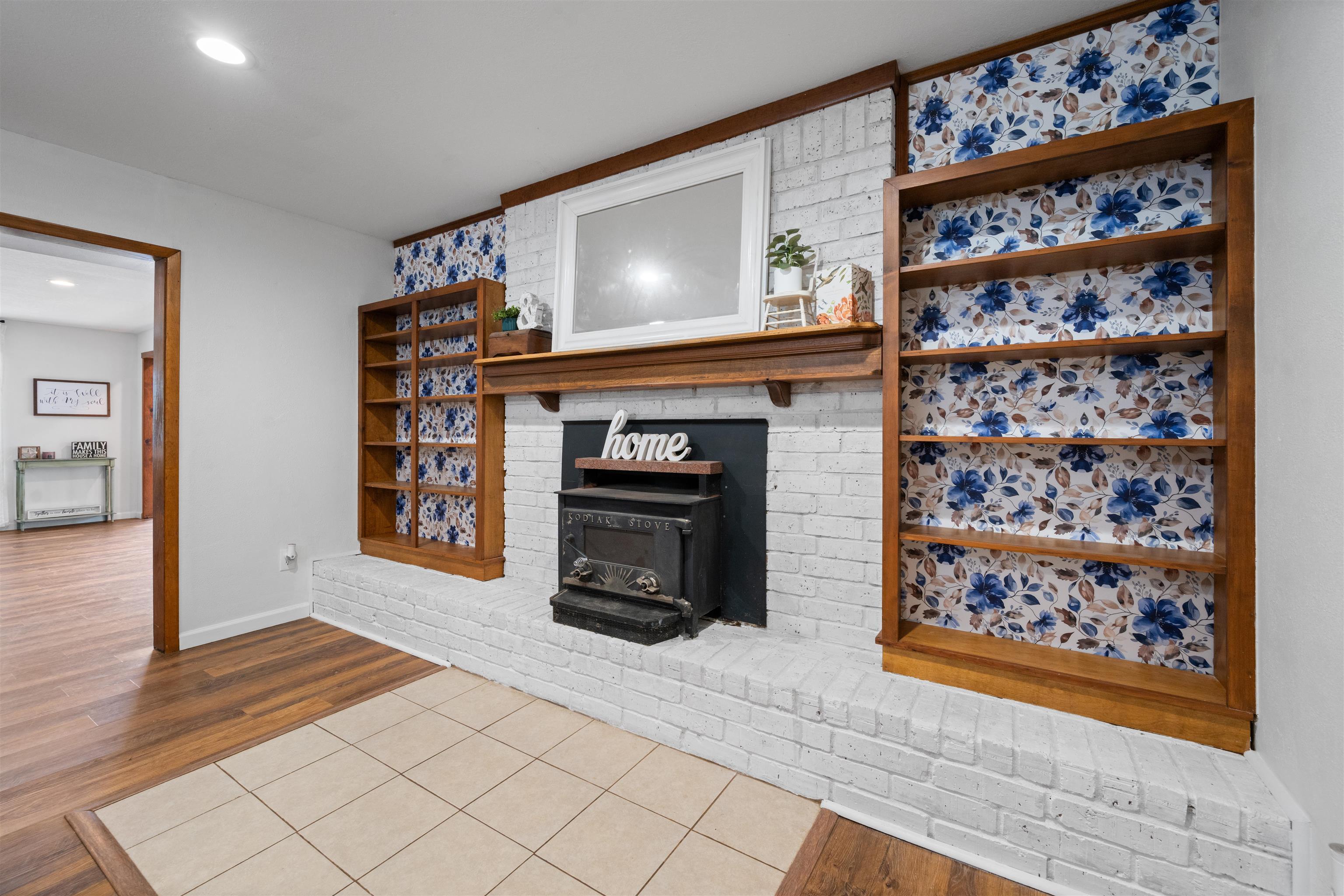 Image 2: White-painted brick fireplace with a wood mantle and a black wood-burning stove, Living Room