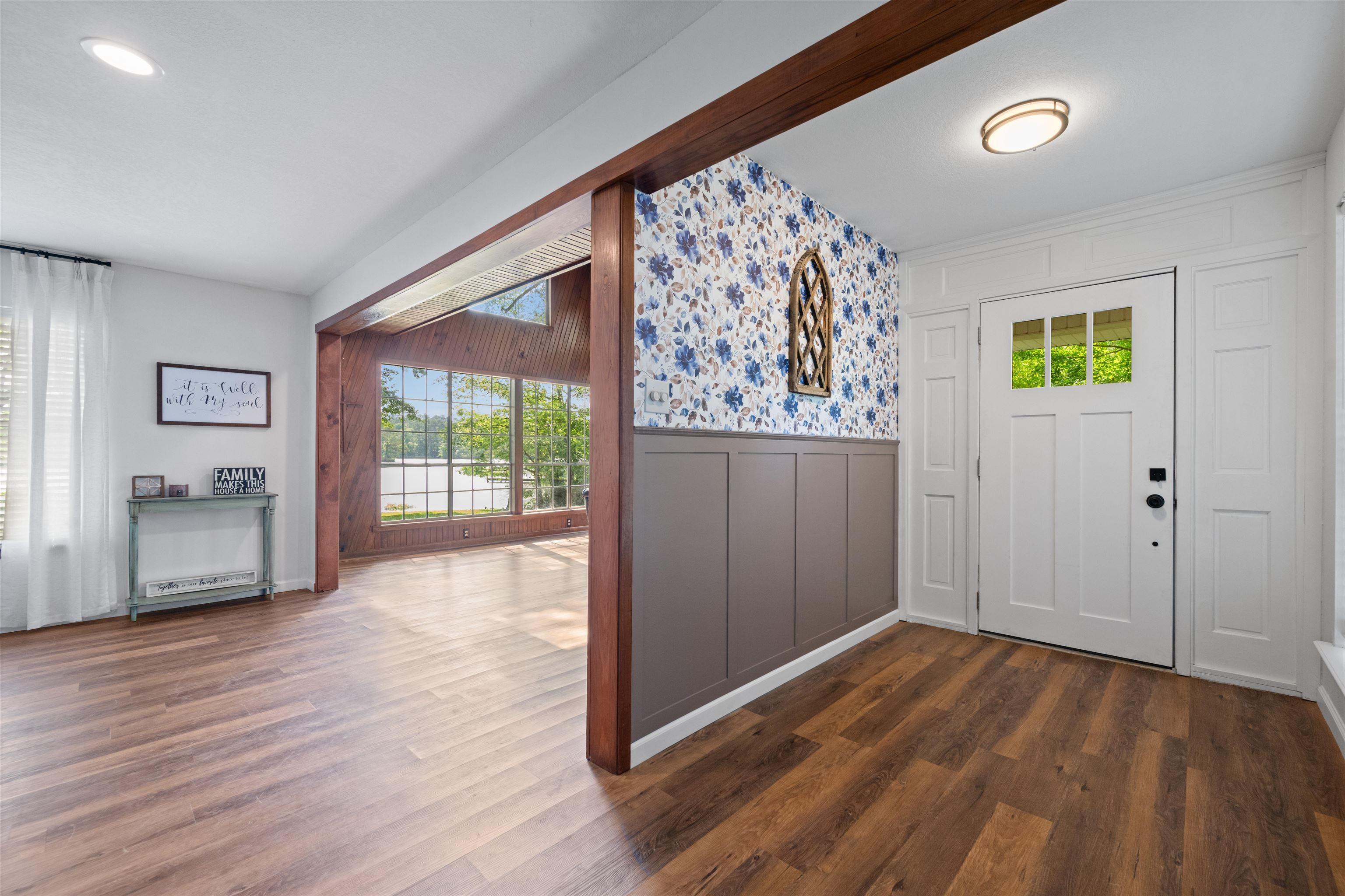 Image 3: Entryway featuring wood-finish flooring, a white paneled door with glass inserts, and a decorative accent wall with floral wallpaper and wainscoting, Entrance Foyer