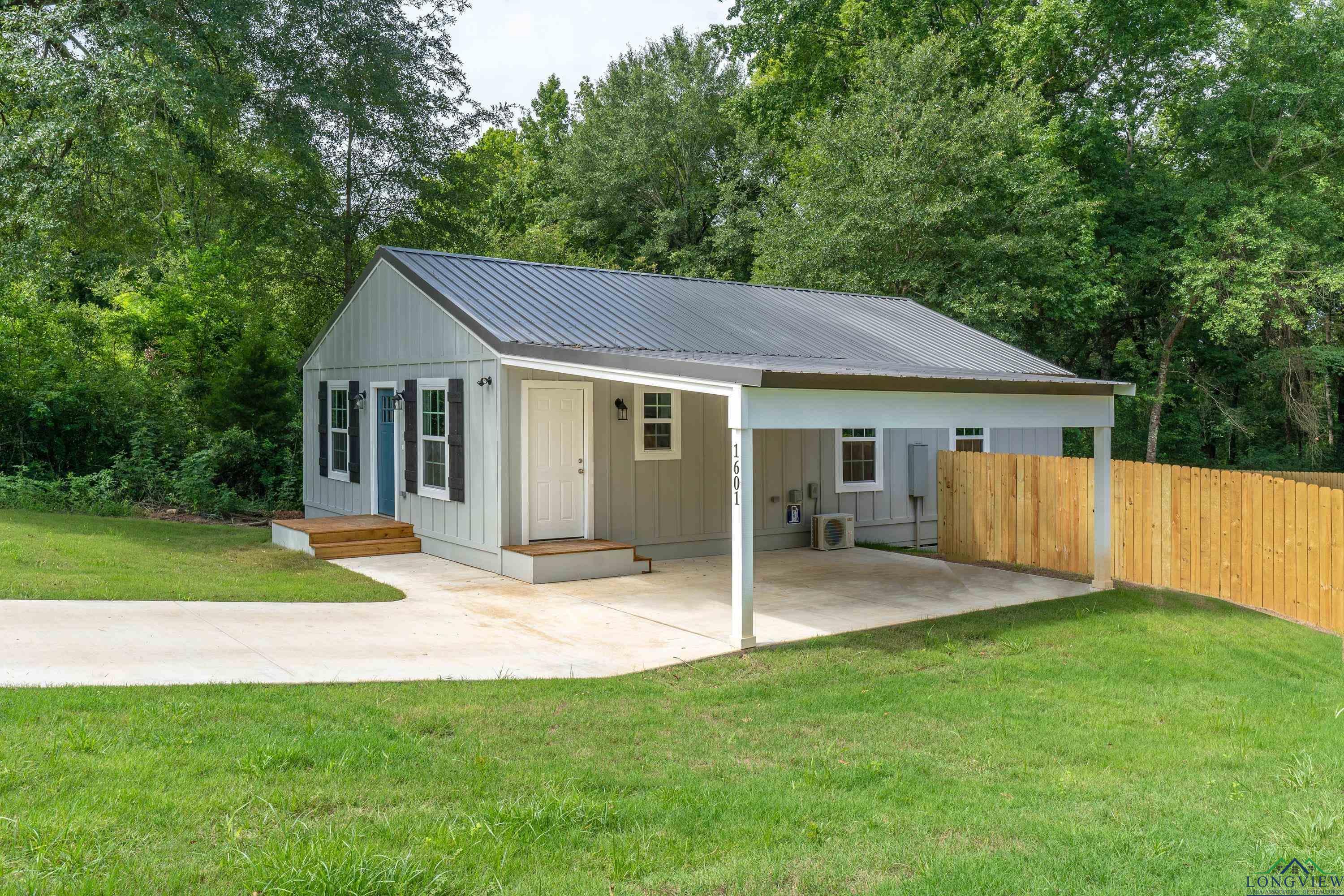 Image 1: View of front of property featuring board and batten siding, a metal roof, a patio area, and view of scattered trees, Front Of Structure