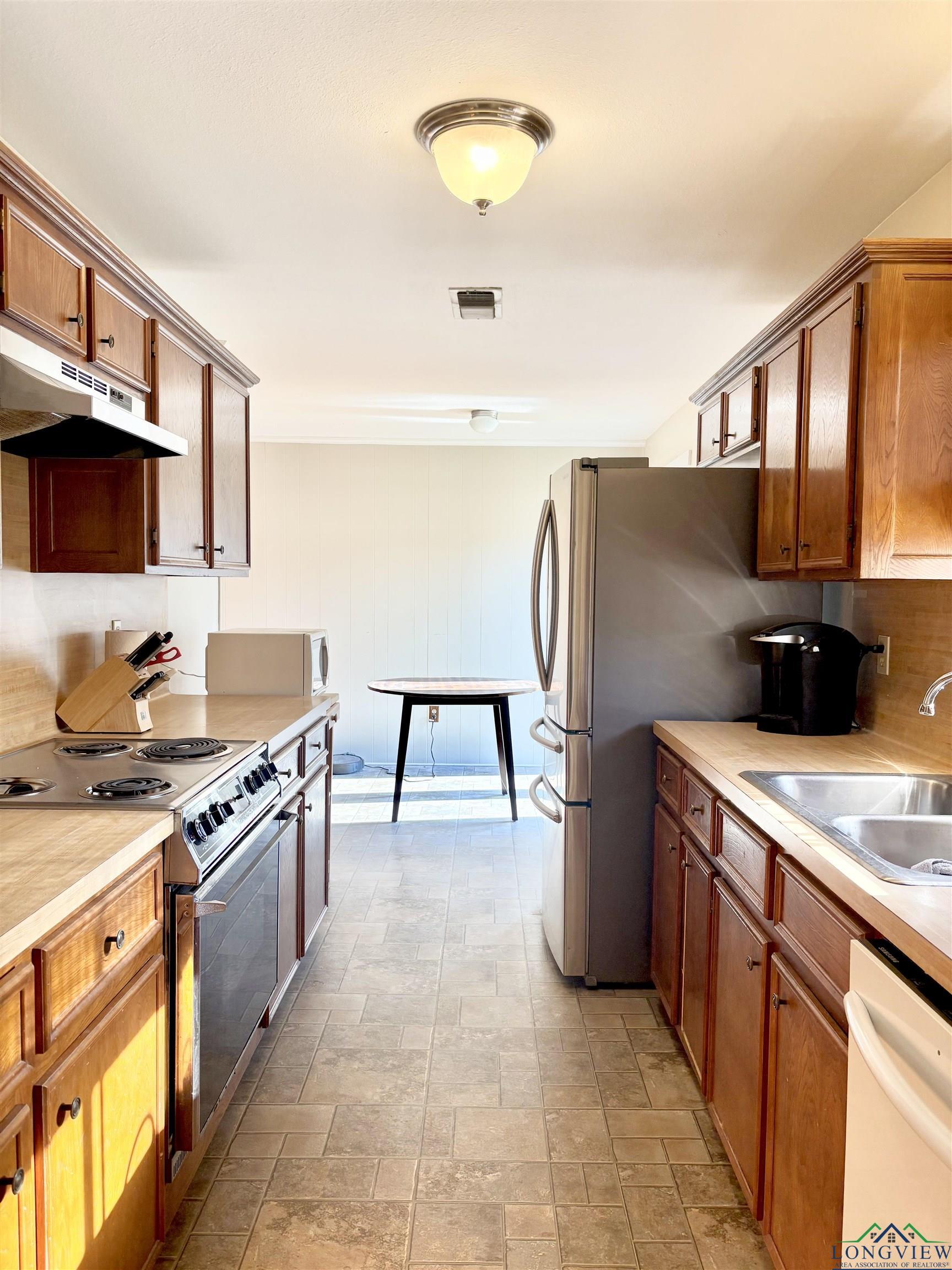 Image 3: Kitchen with appliances with stainless steel finishes, brown cabinets, light countertops, under cabinet range hood, and stone finish flooring, Kitchen
