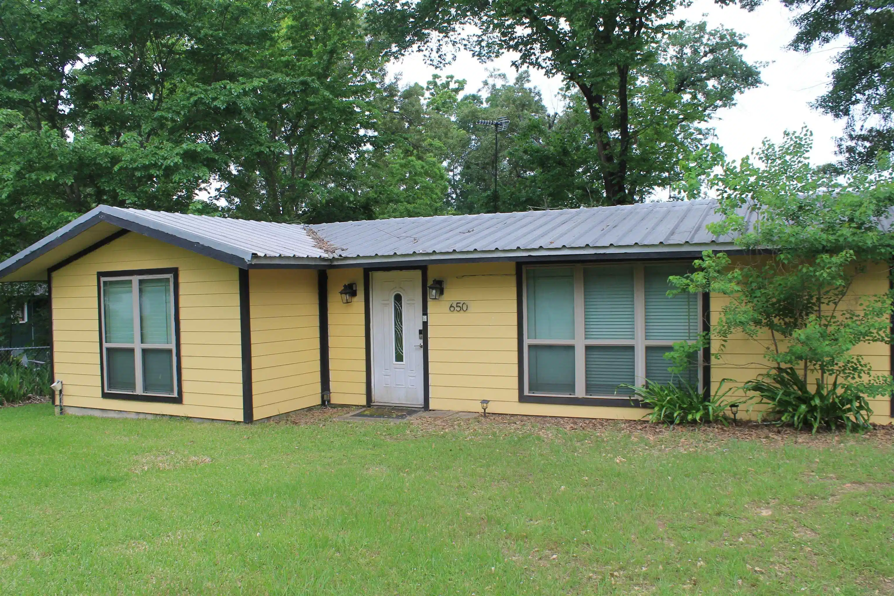 Image 0: Single-story residence featuring yellow siding, a gray metal roof, and dark trim, Front Of Structure