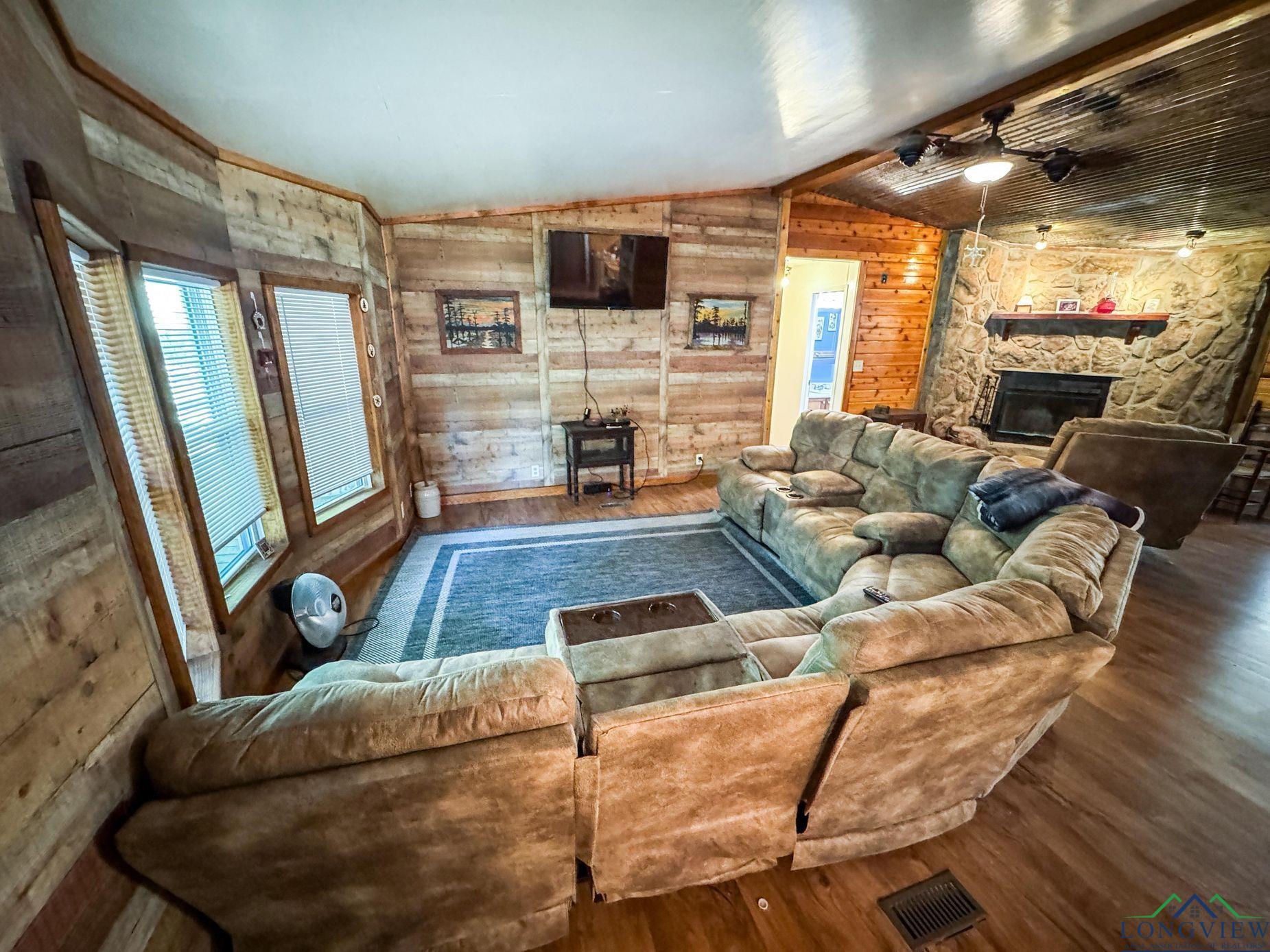 Image 2: Living area with wood finished floors, wooden walls, lofted ceiling, and a fireplace, Living Room