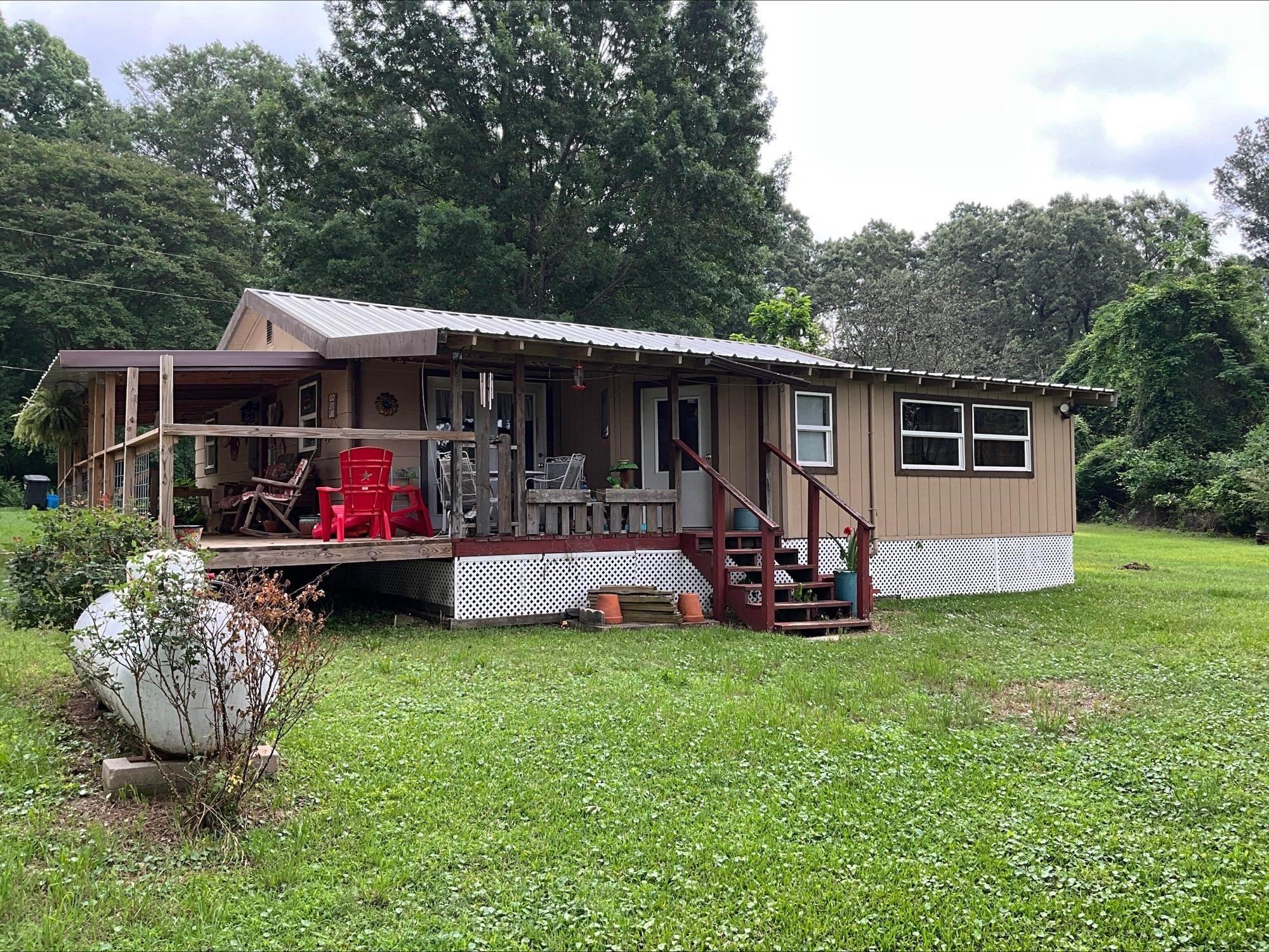 Image 3: Single-story residence featuring a covered wooden deck, white lattice skirting, and a metal roof, Front Of Structure