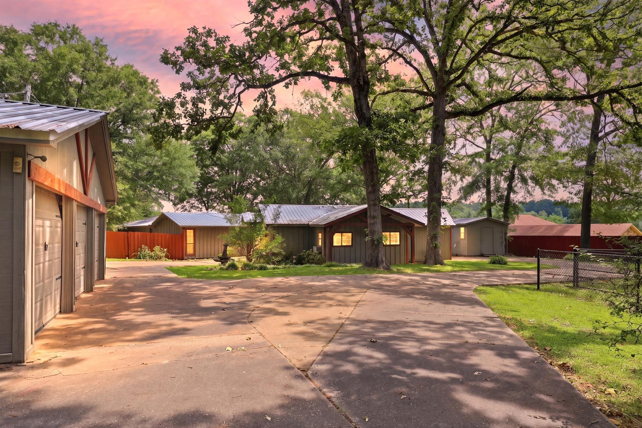 Image 1: Extensive concrete driveway leading to multiple structures, including a three-bay garage with overhead doors, a primary residence with board-and-batten siding, and additional outbuildings, Front Of Structure