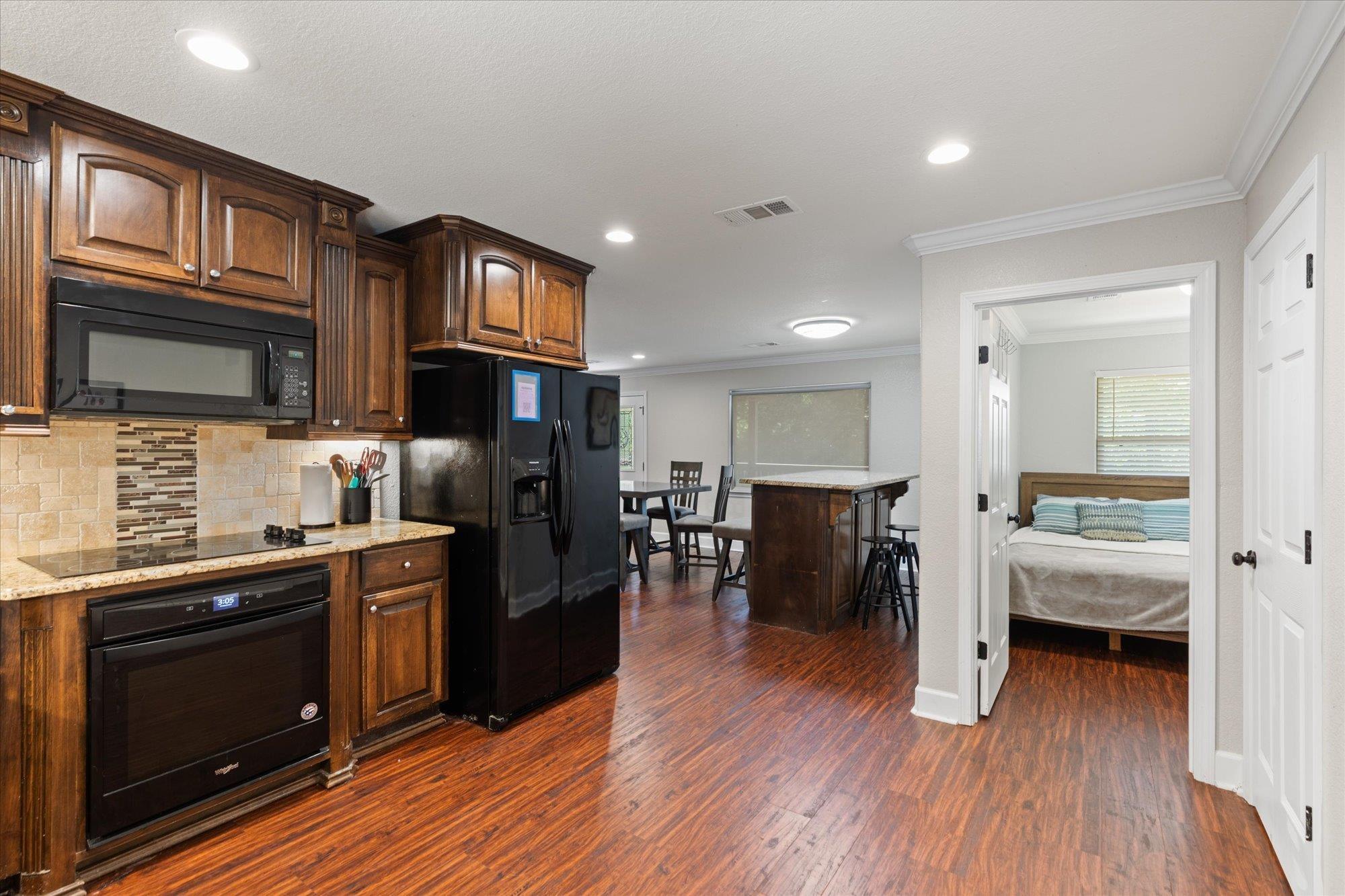 Image 1: Open-concept kitchen featuring wood cabinetry, black appliances, light-toned countertops, and a tiled backsplash, Kitchen