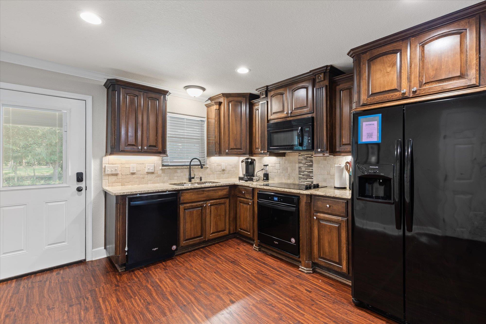 Image 3: Kitchen featuring rich wood cabinetry, granite countertops, a tiled backsplash, and wood-finish flooring, Kitchen