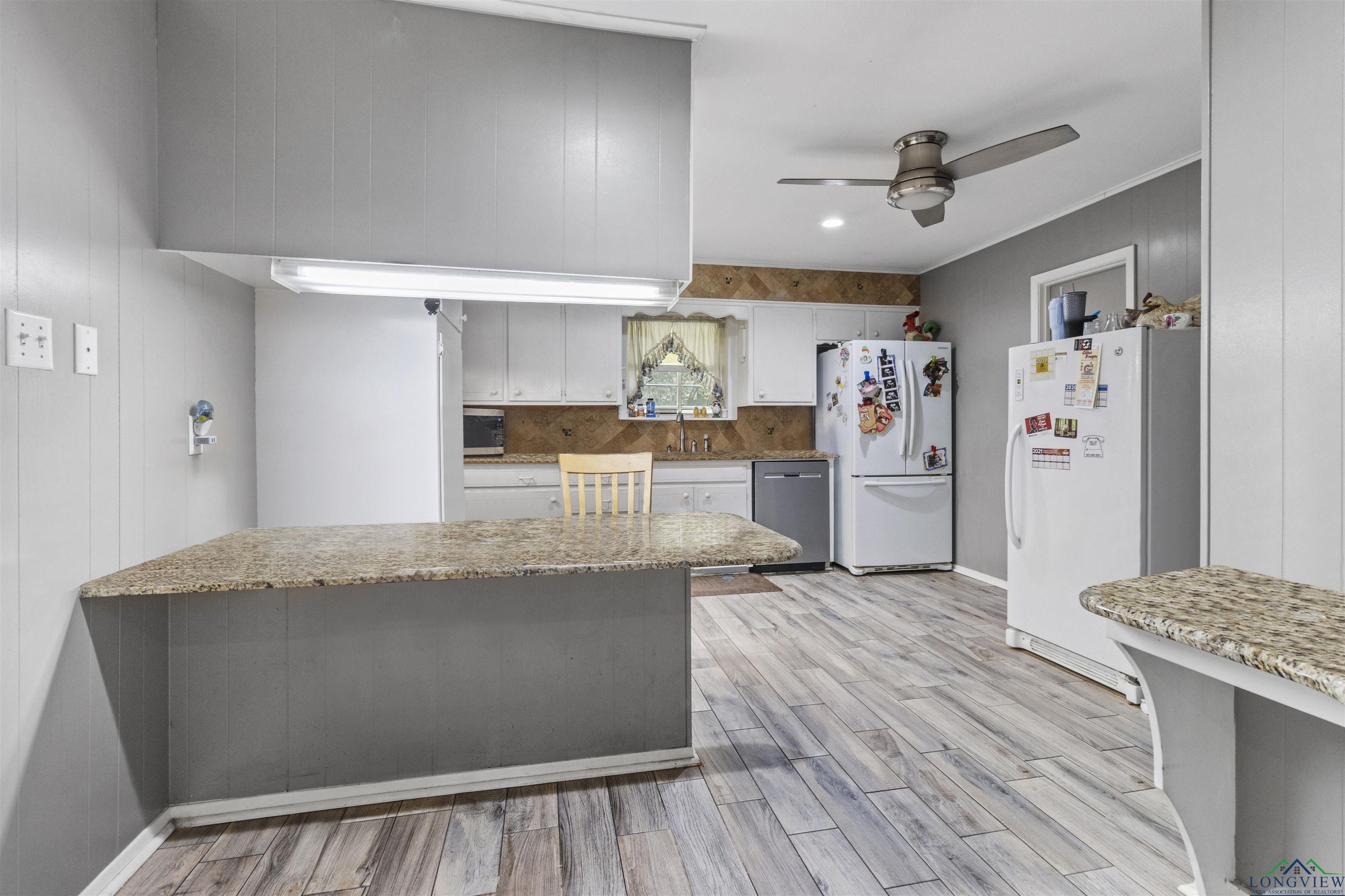 Image 3: Kitchen featuring stainless steel appliances, white cabinetry, light wood-type flooring, light stone counters, and wood walls, Kitchen