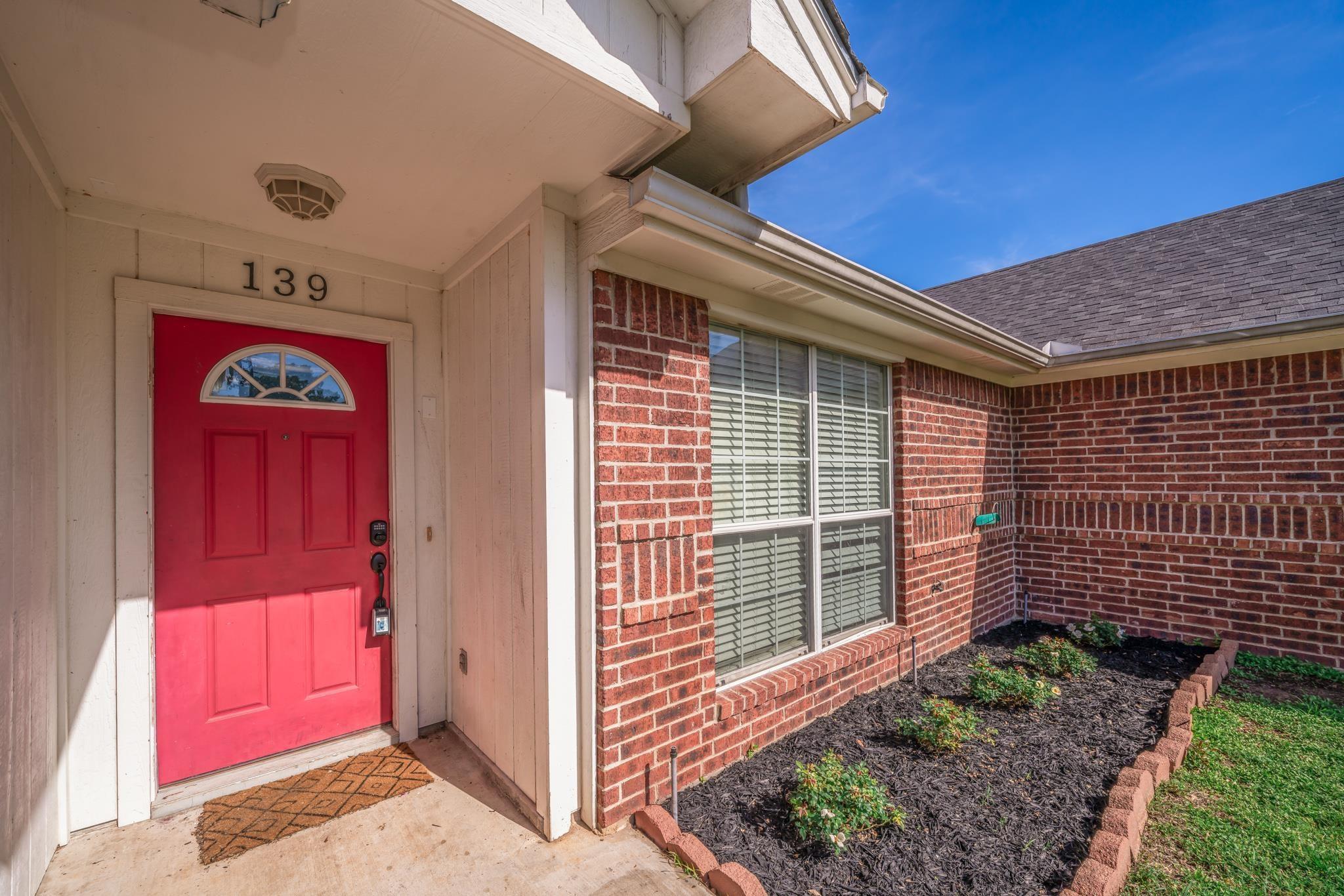 Image 2: Entryway featuring a vibrant red paneled door with an arched transom window, brick exterior, white trim, and a landscaped garden bed, Entry