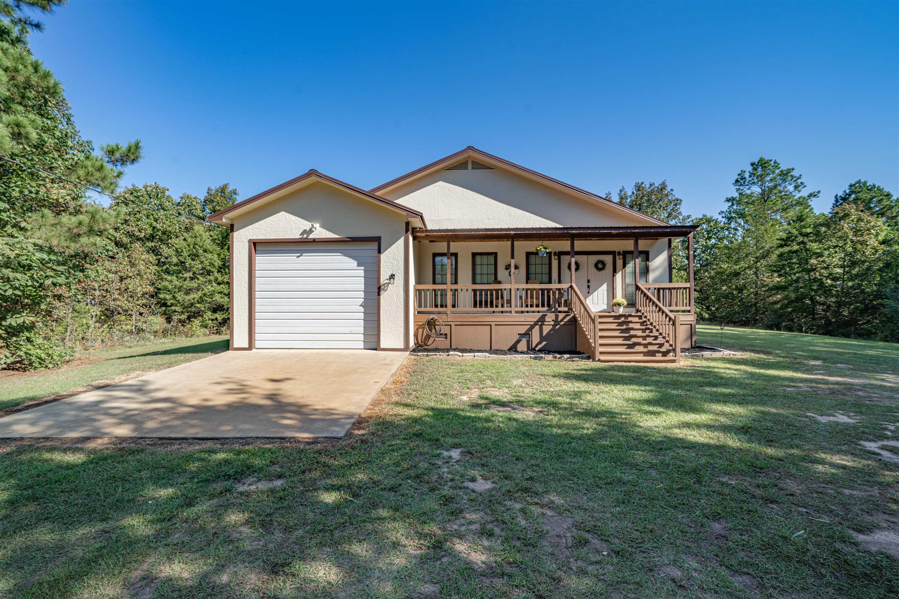 Image 0: View of front facade featuring covered porch, stucco siding, a front yard, stairs, and an attached garage, Front Of Structure