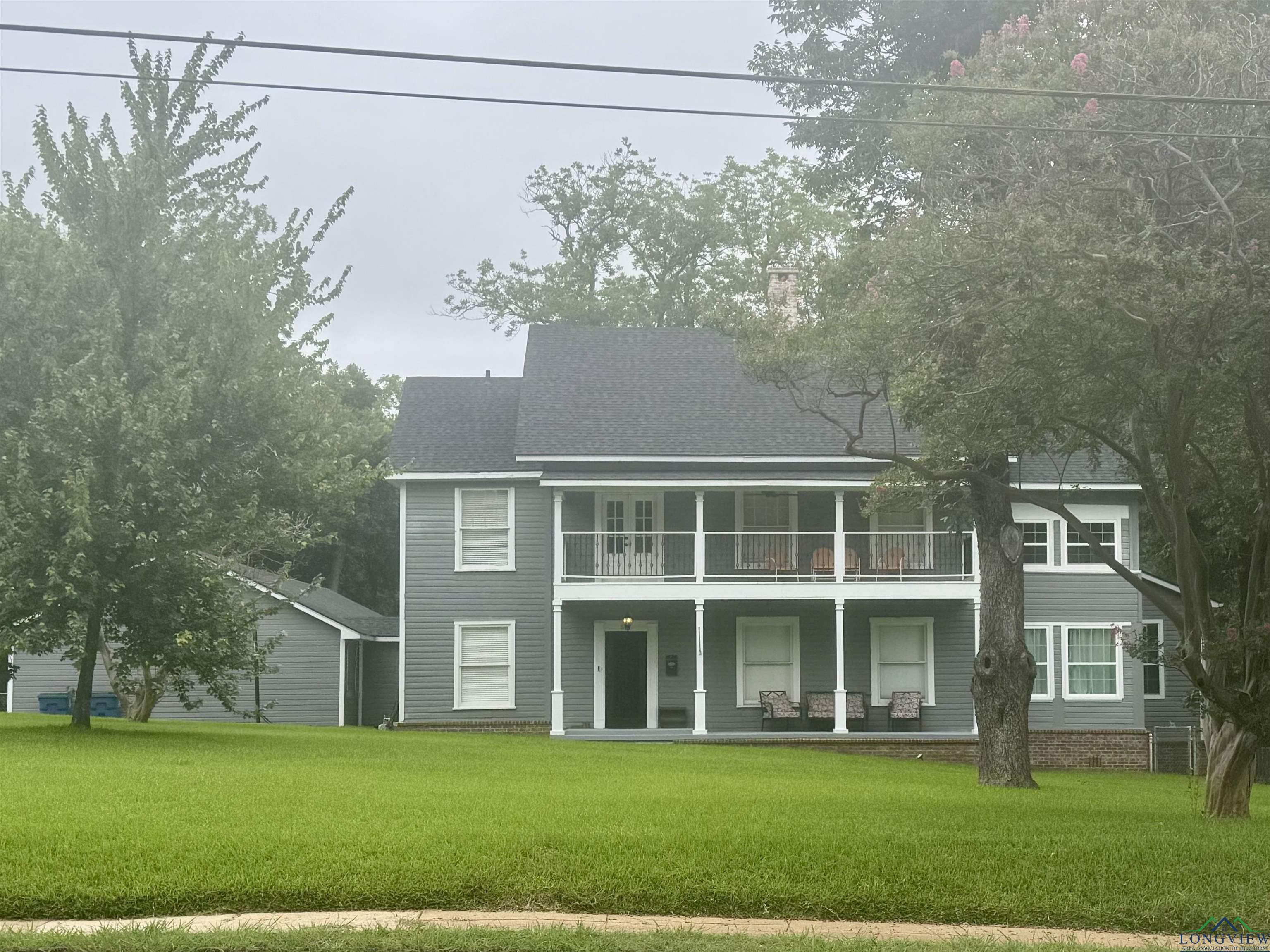 Image 0: Back of property featuring a balcony, a shingled roof, a lawn, and a porch, Back Of Structure