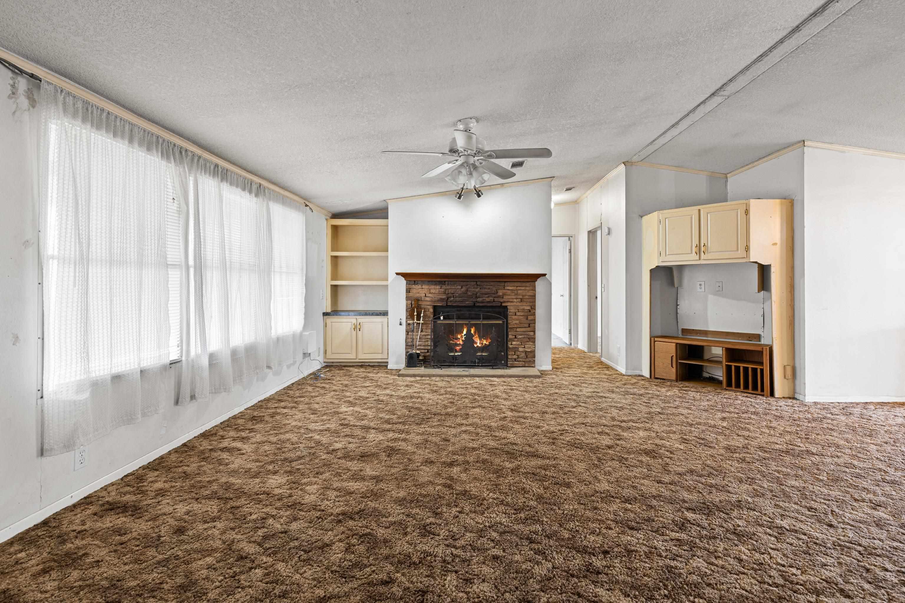 Image 3: Unfurnished living room with a textured ceiling, a lit fireplace, dark colored carpet, lofted ceiling, and ceiling fan, Living Room