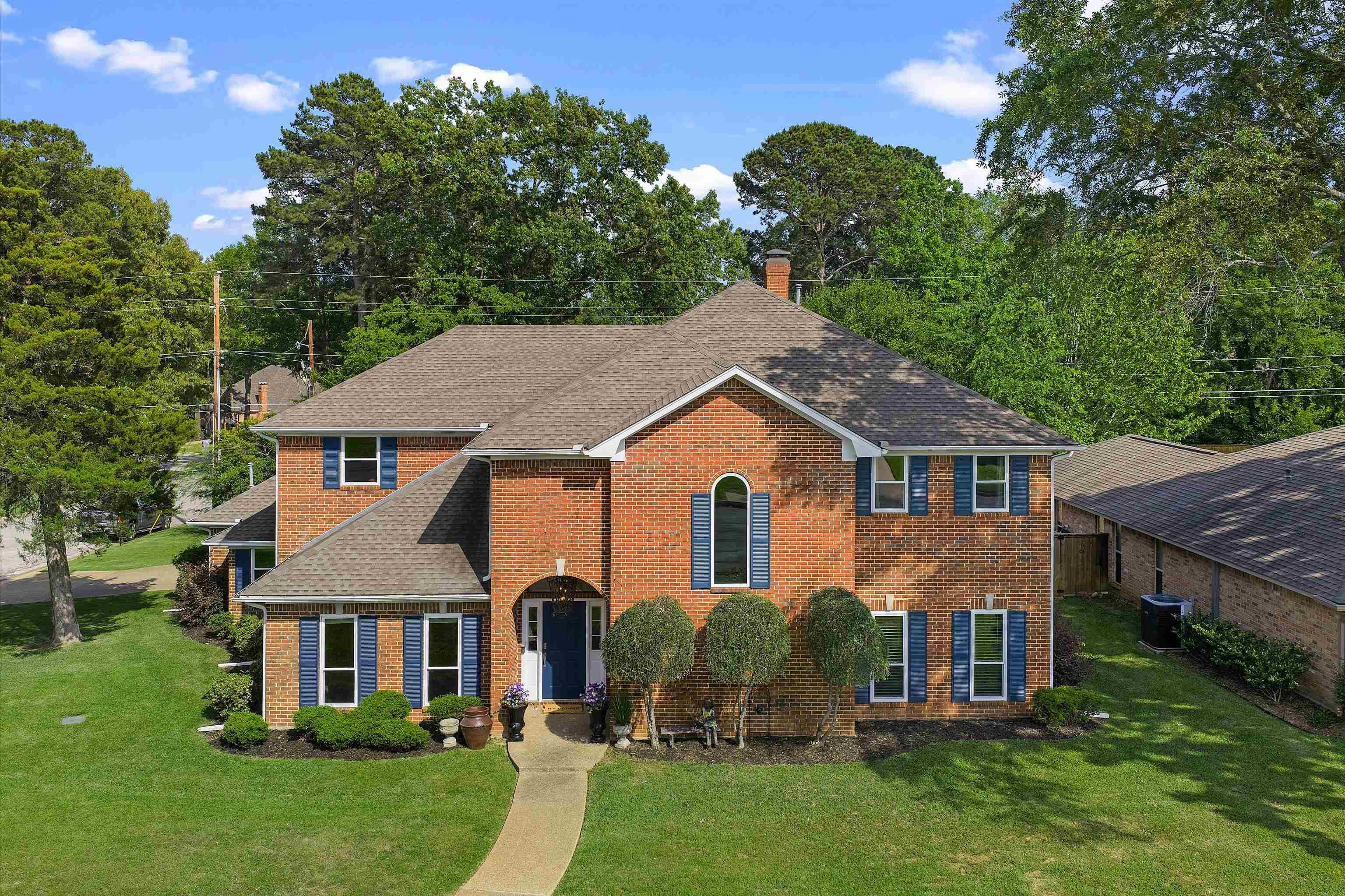 Image 0: Traditional brick exterior featuring blue window shutters, an arched entryway, a gabled roofline, a paved walkway, and mature landscaping, Front Of Structure