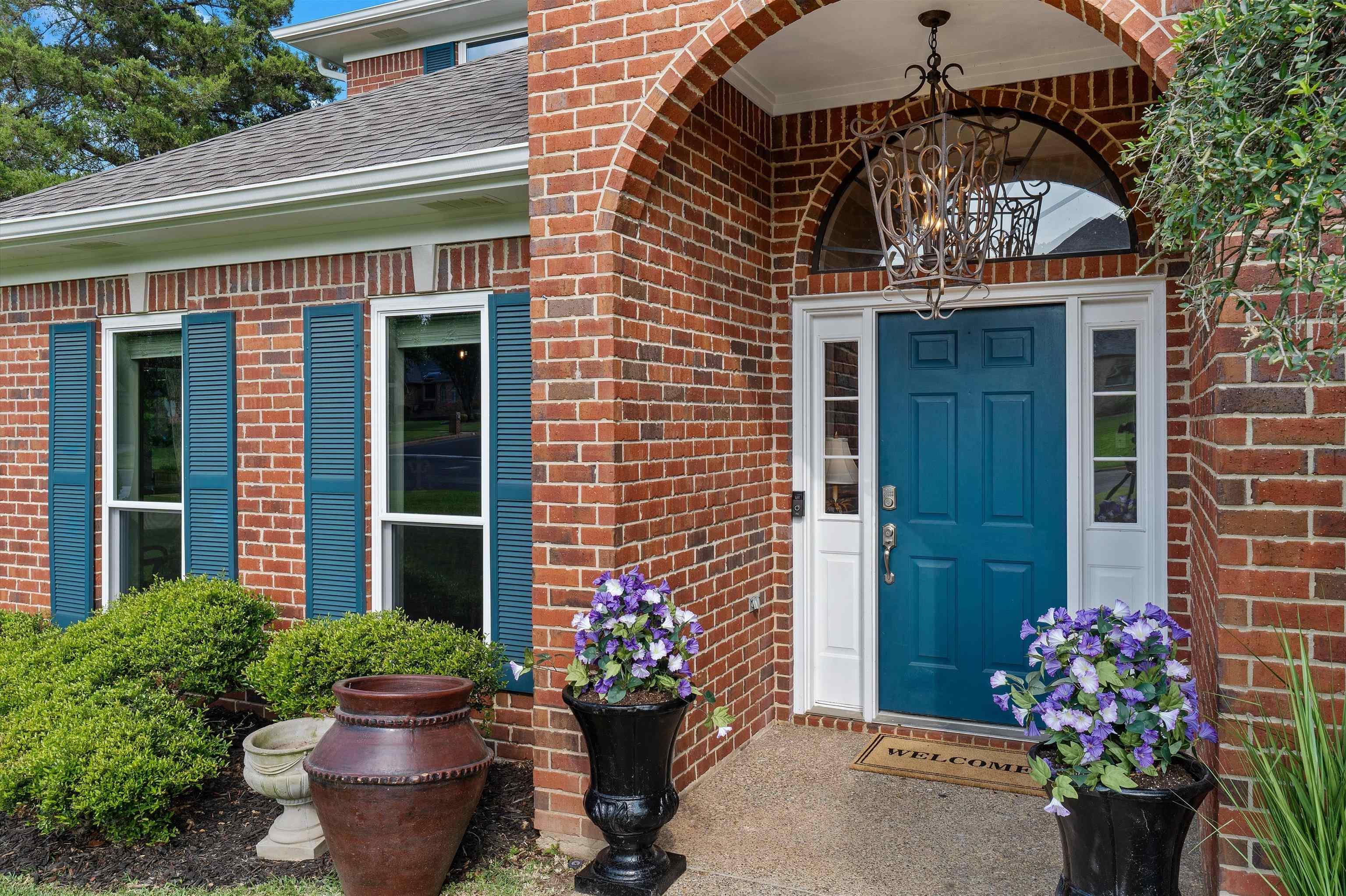 Image 1: Brick exterior featuring an arched entryway with an ornate chandelier, a paneled blue entry door, and white sidelights, Entry