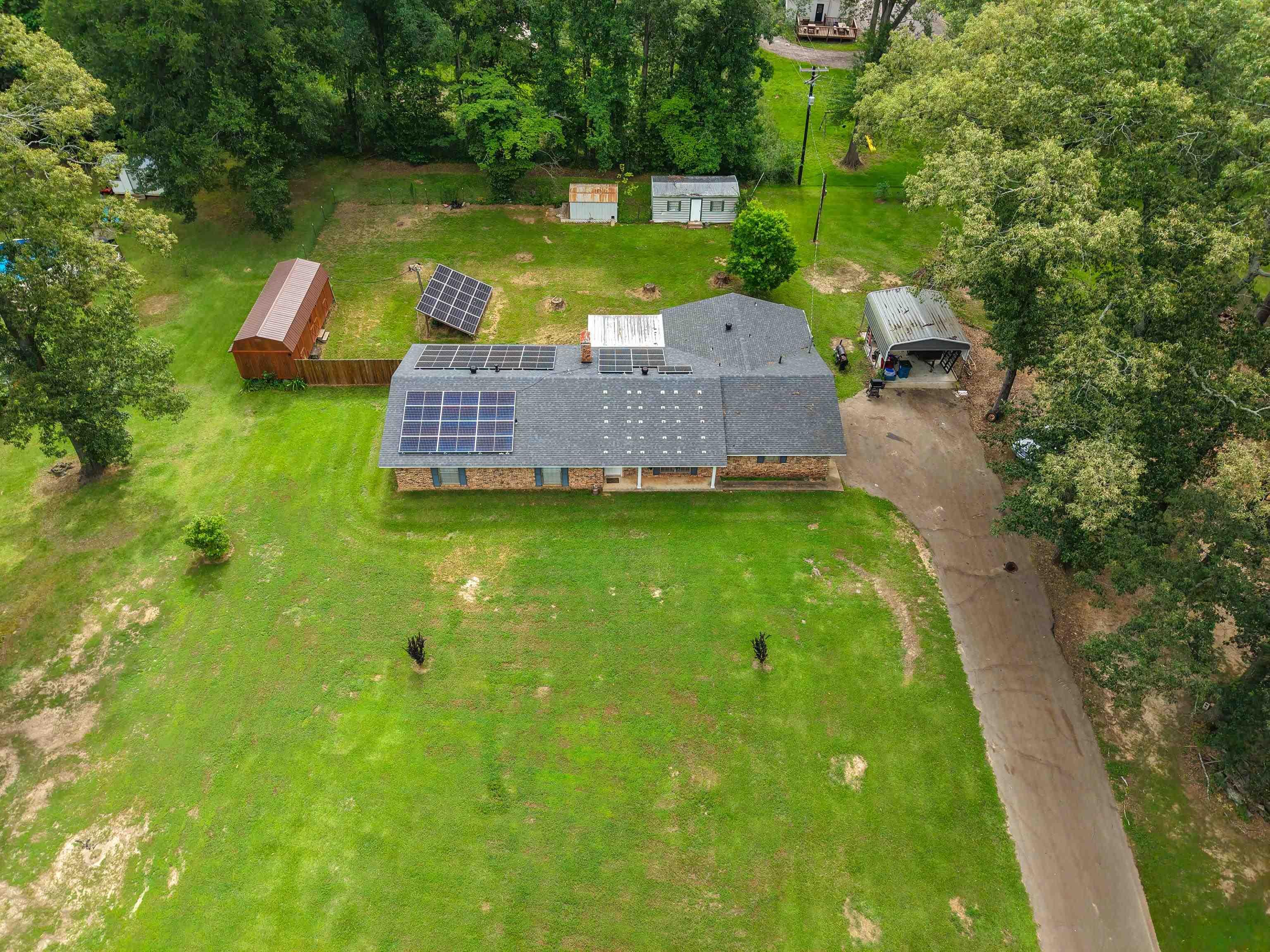 Image 1: Ranch-style residence featuring a dark shingle roof with integrated solar panels, Aerial View