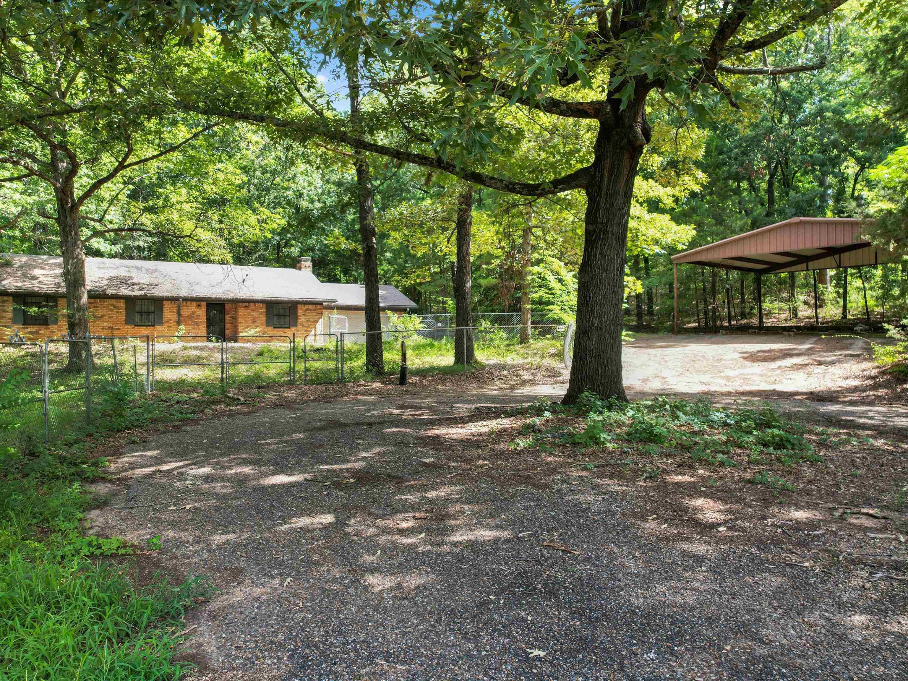 Image 0: View of yard with driveway, a detached carport, and a forest view, Yard