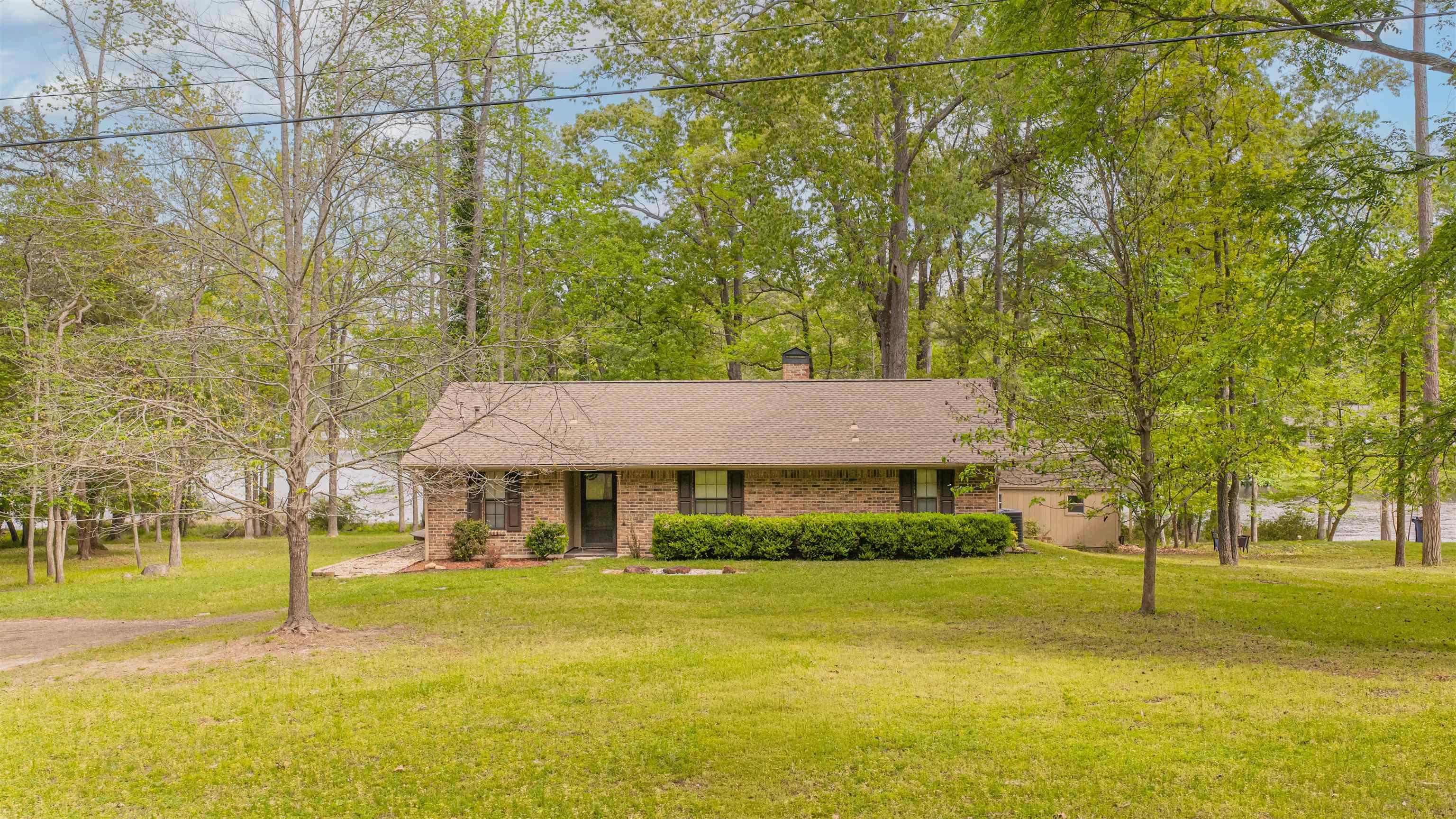 Image 1: Ranch-style home featuring a front yard, a shingled roof, covered porch, brick siding, and a chimney, Front Of Structure
