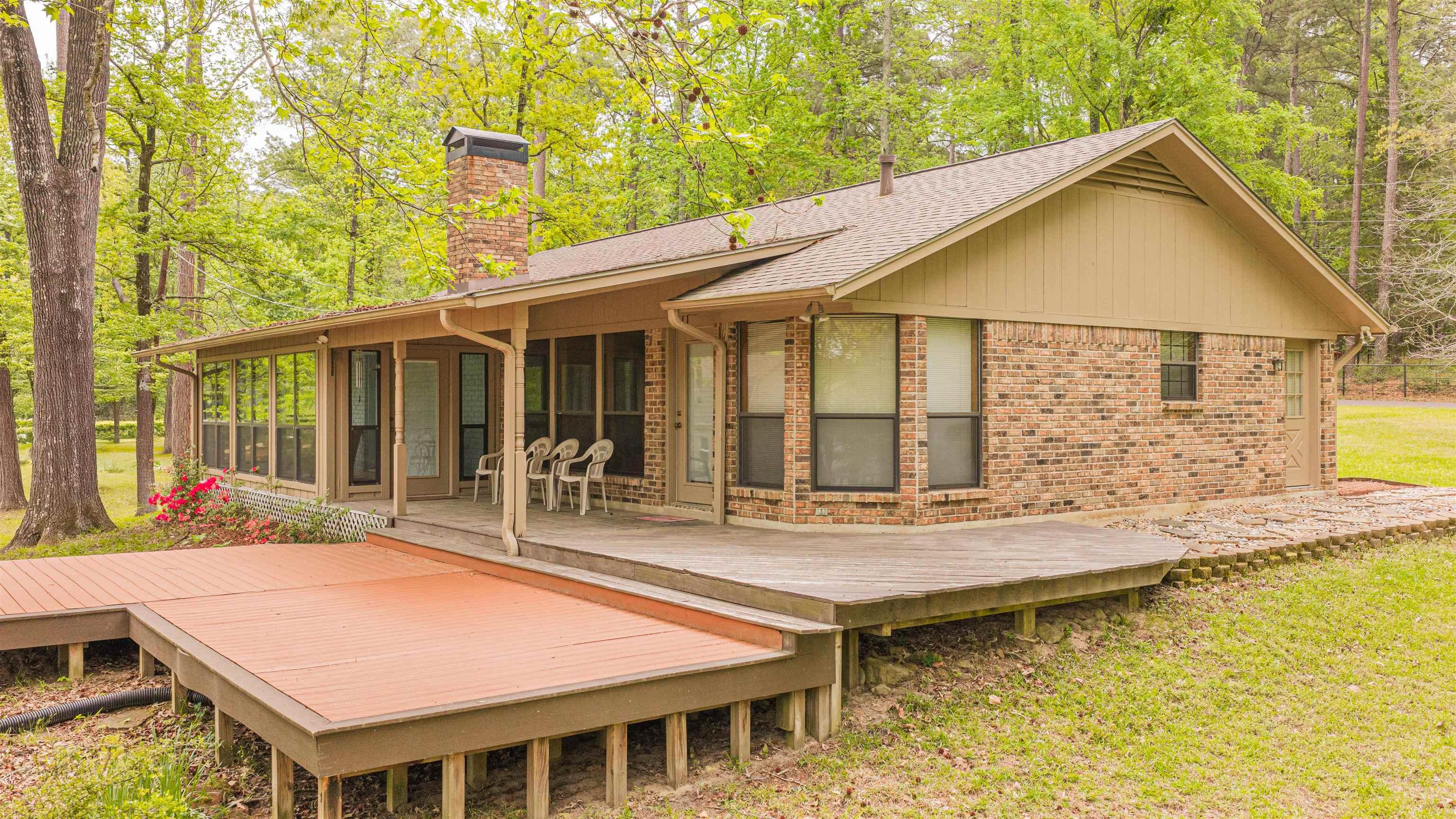 Image 2: Back of property featuring a sunroom, a wooden deck, brick siding, and a chimney, Back Of Structure