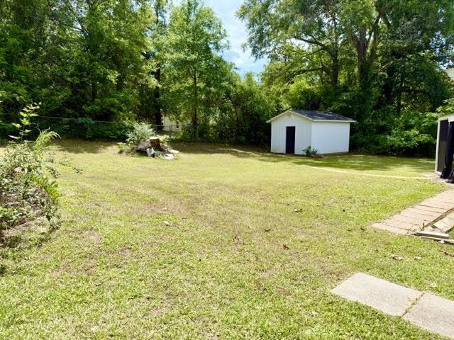 Image 2: Expansive backyard featuring a manicured lawn, mature trees, a white storage shed with dark trim, and a paved walkway, Yard