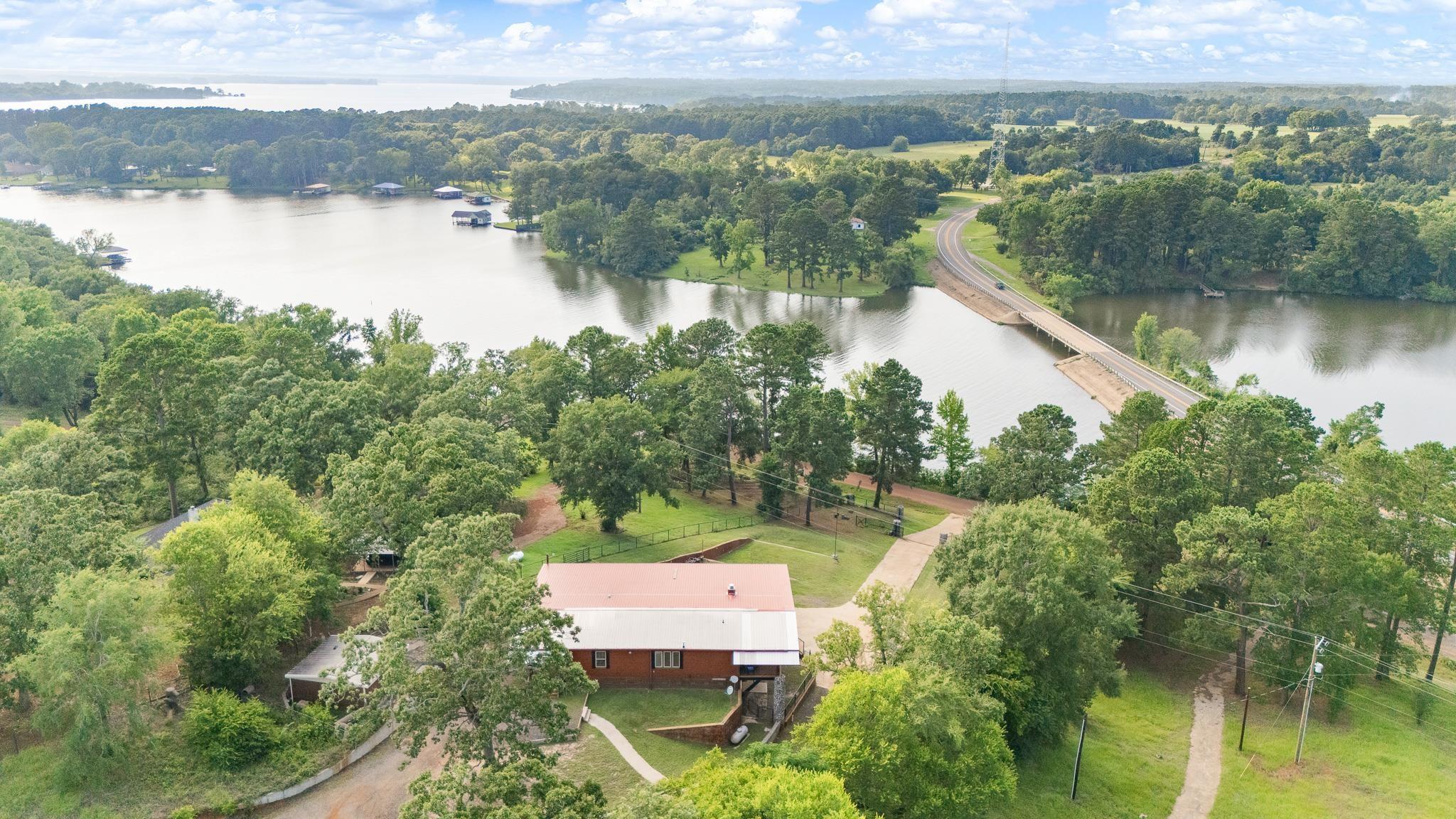 Image 3: Aerial perspective showcasing a waterfront property with extensive tree coverage and a visible red-roofed structure, Aerial View