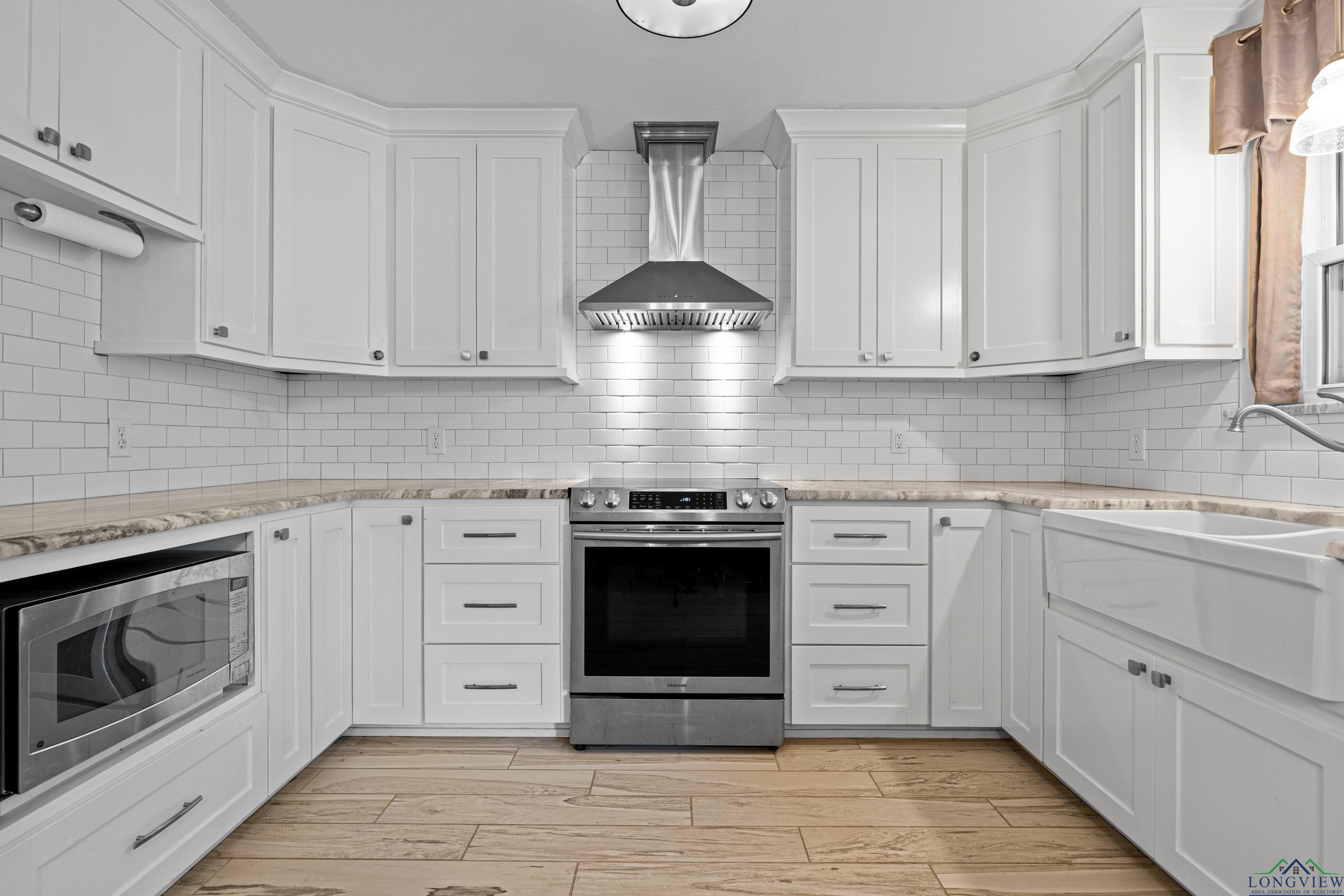 Image 1: Kitchen featuring appliances with stainless steel finishes, wall chimney exhaust hood, white cabinets, and decorative backsplash, Kitchen