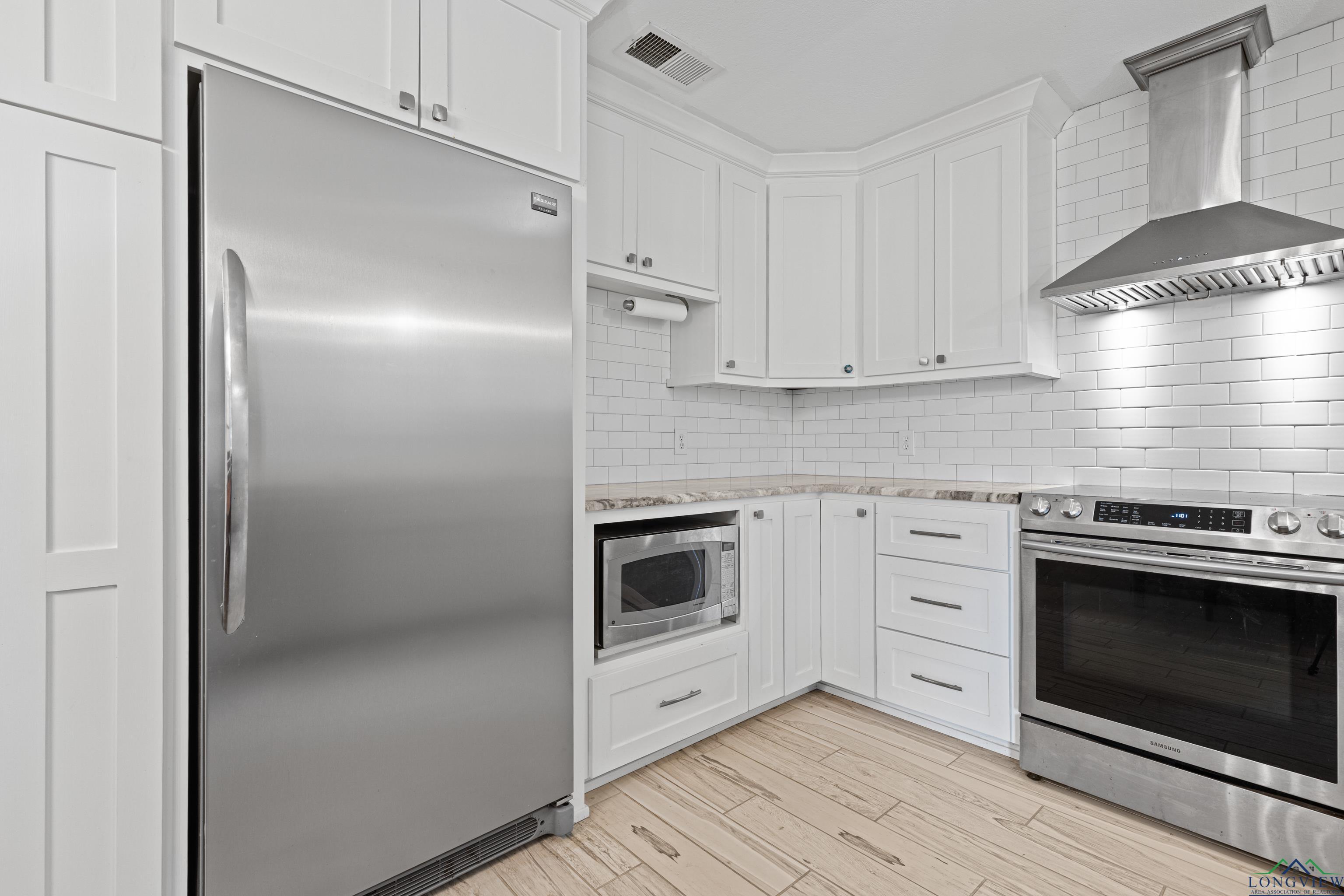 Image 2: Kitchen featuring stainless steel appliances, wall chimney exhaust hood, white cabinetry, and backsplash, Kitchen