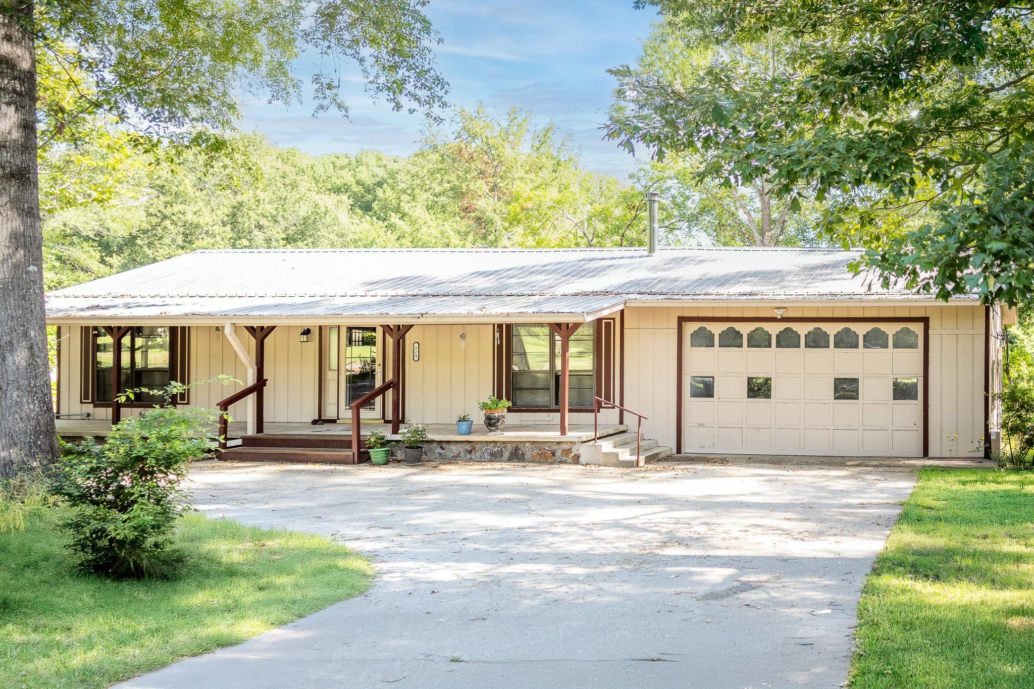 Image 1: View of front of house featuring a porch, driveway, a metal roof, and an attached garage, Front Of Structure