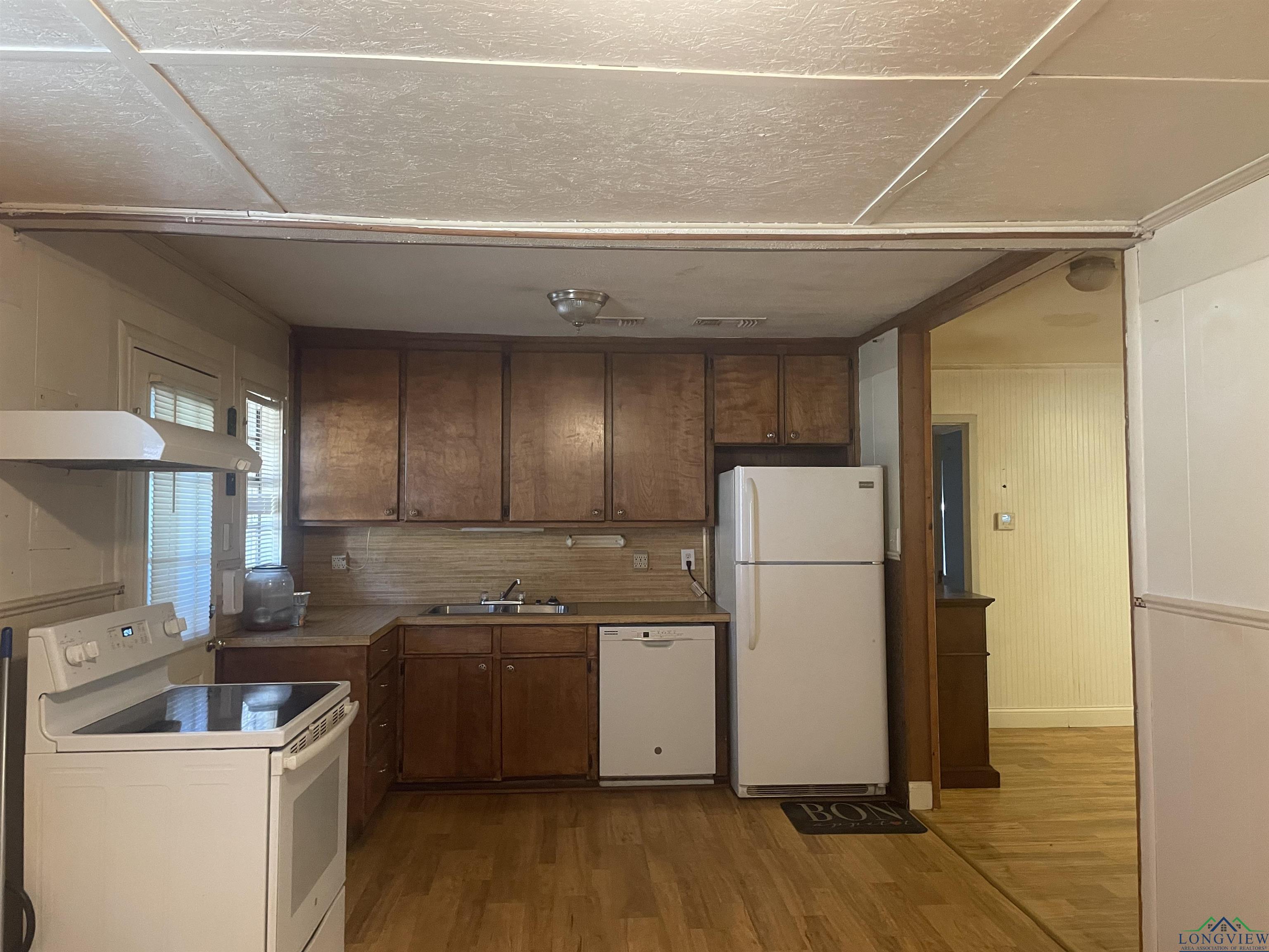 Image 1: Kitchen with white appliances, dark wood-style floors, backsplash, under cabinet range hood, and light countertops, Kitchen