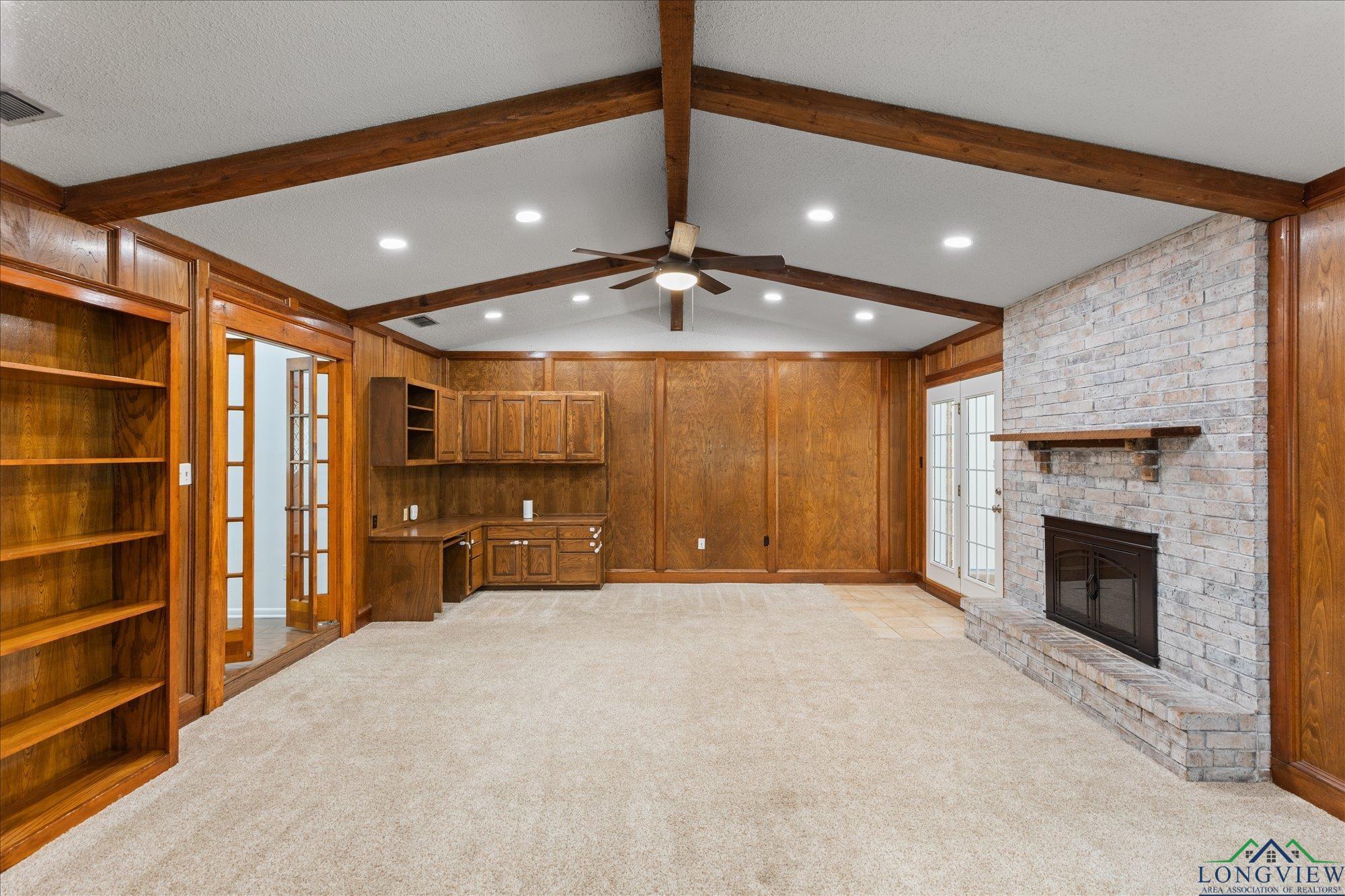 Image 1: Unfurnished living room featuring wooden walls, built in study area, french doors, light carpet, and a fireplace, Living Room