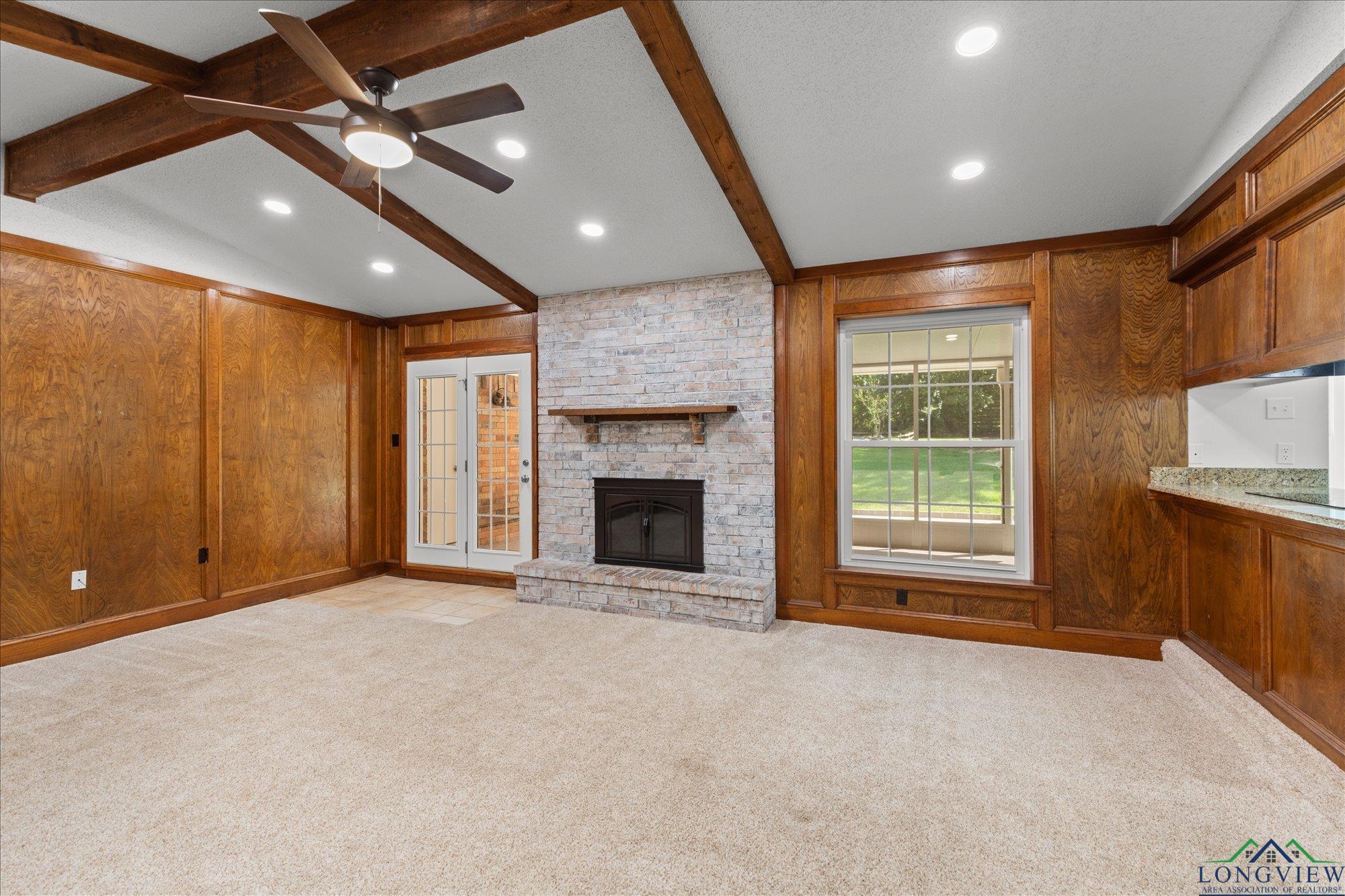 Image 2: Unfurnished living room with wooden walls, light colored carpet, a brick fireplace, a ceiling fan, and recessed lighting, Living Room