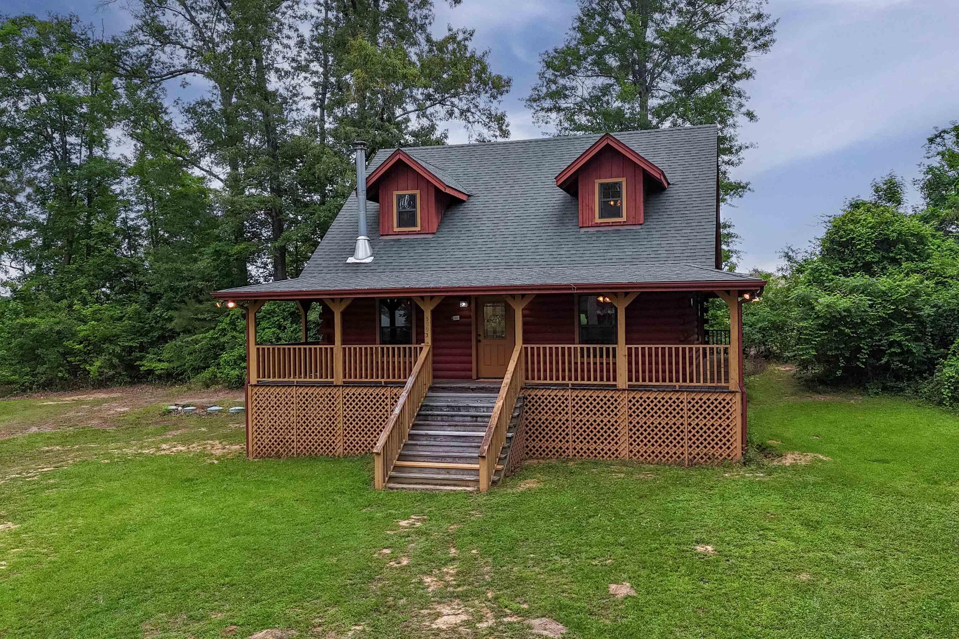 Image 1: Red log cabin exterior with a full-width covered front porch, Front Of Structure