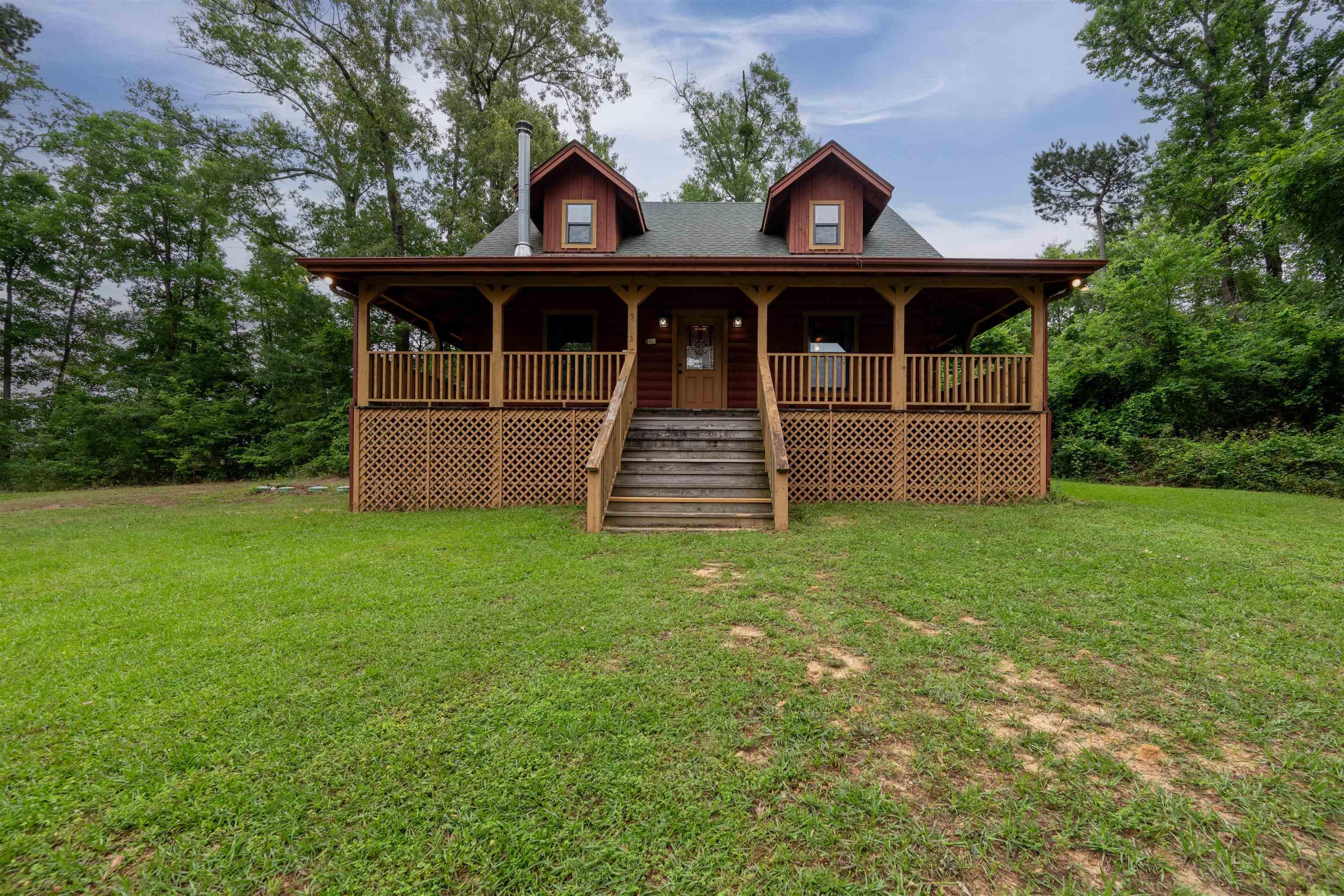 Image 2: Wood-sided cabin-style residence featuring a wrap-around porch with wooden railing and lattice skirting, a multi-pane front door, and a chimney, Front Of Structure