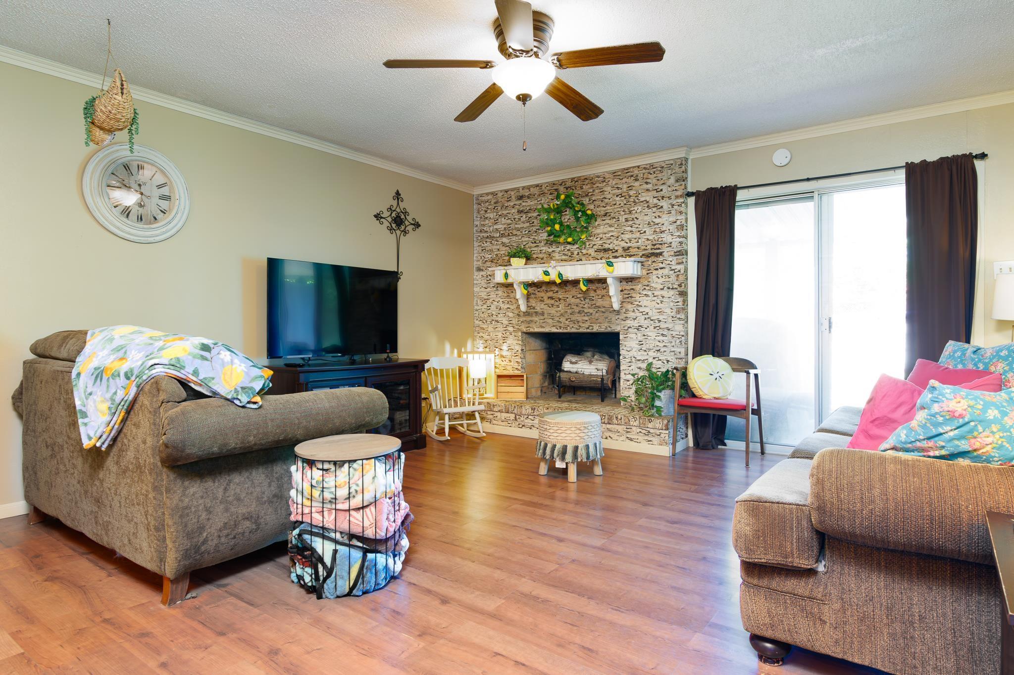Image 3: Living area featuring wood-finish flooring, a stone-clad fireplace with a white mantel, and a ceiling fan with integrated lighting, Living Room