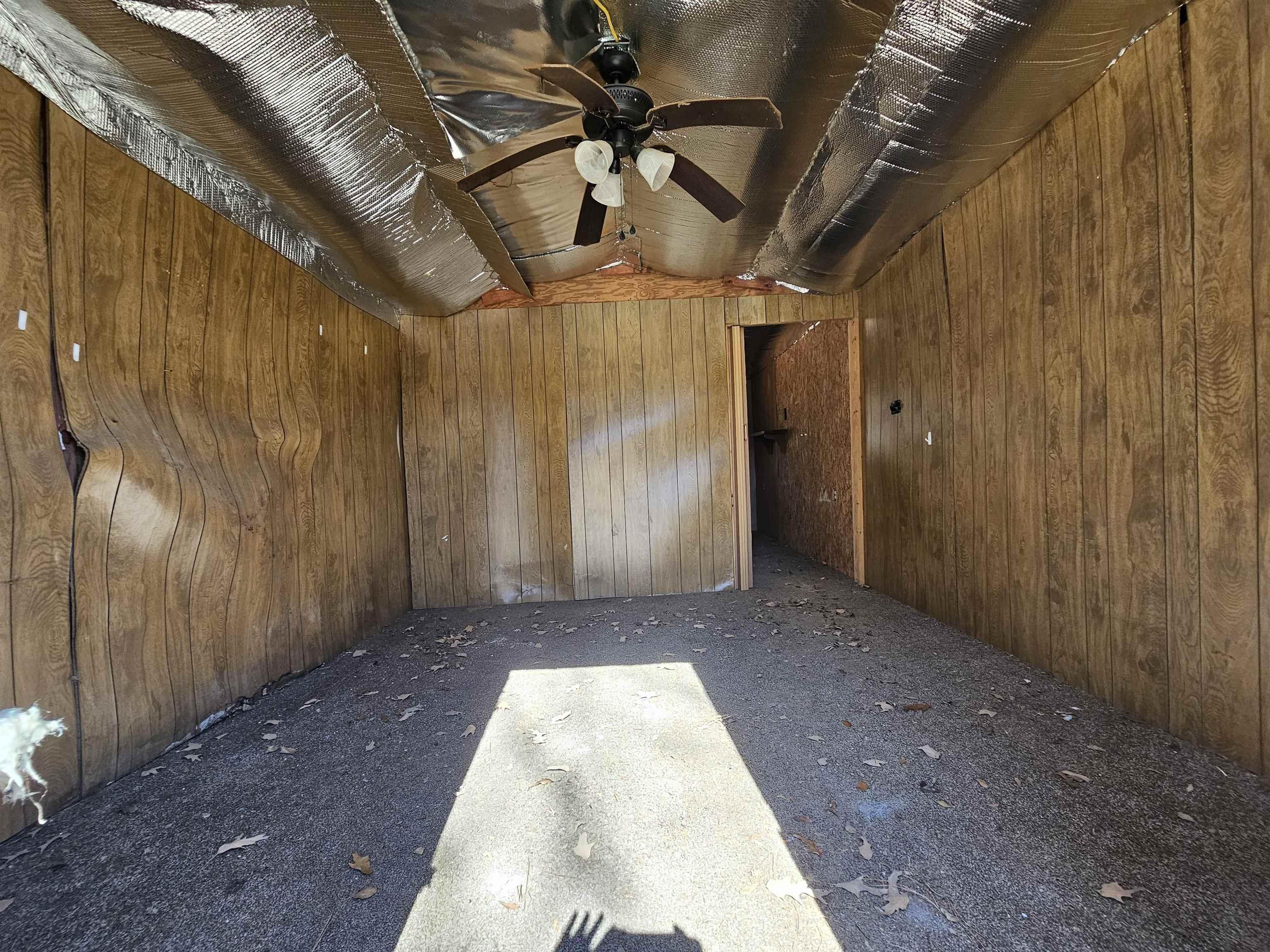 Image 3: Wood-paneled interior walls with a textured ceiling featuring exposed insulation and a ceiling fan, Other