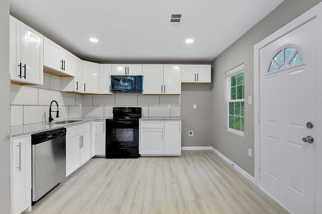 Image 3: Kitchen featuring white cabinetry with black hardware, stone-finish countertops, and a subway tile backsplash, Kitchen