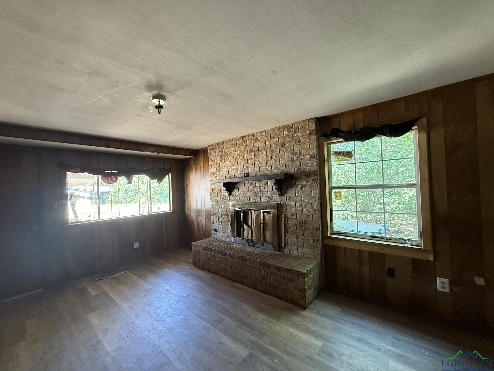 Image 3: Unfurnished living room with wooden walls, a brick fireplace, and wood finished floors, Living Room