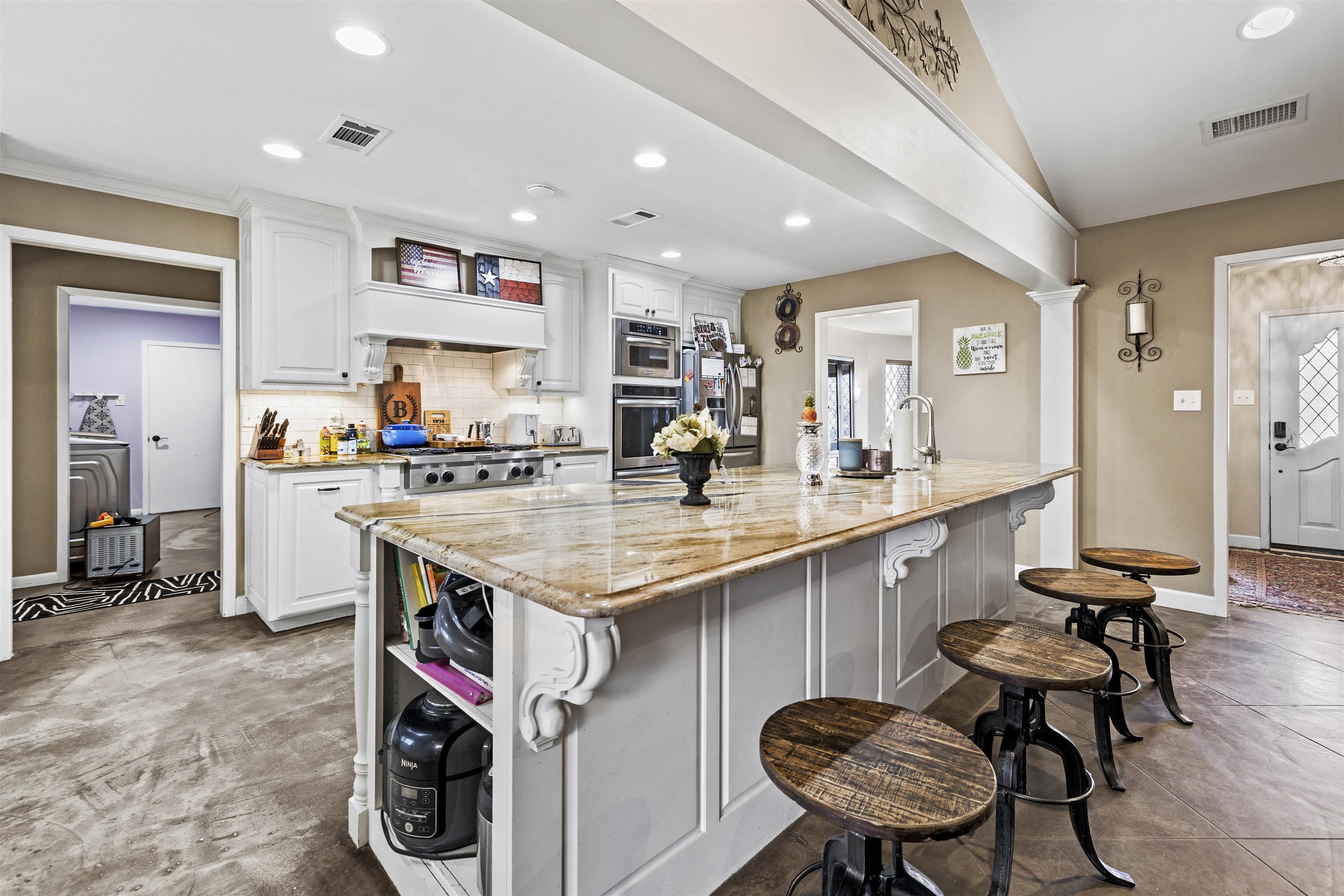 Image 3: Kitchen featuring light stone counters, a breakfast bar area, white cabinets, a kitchen island with sink, and decorative backsplash, Kitchen