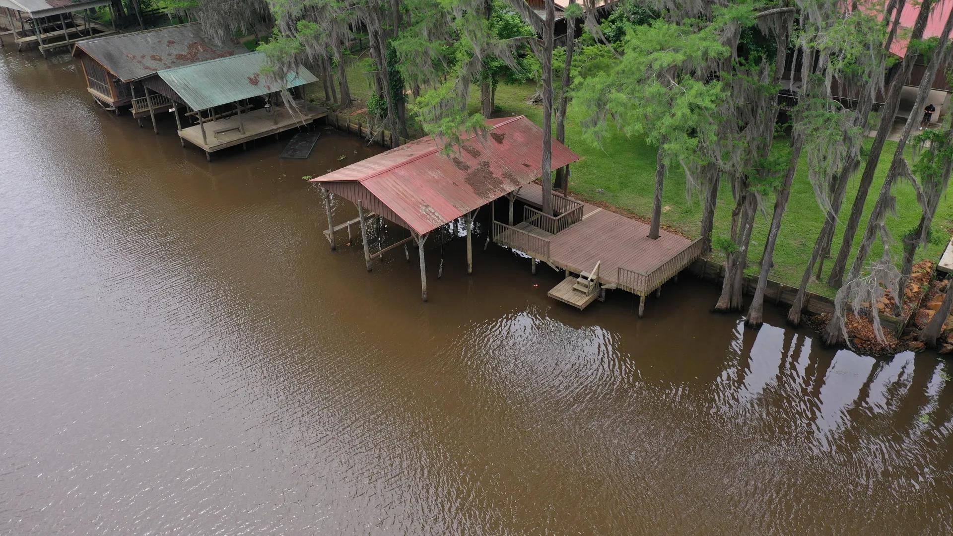 Image 3: Waterfront property featuring a private boat dock with a covered slip, an expansive wood-finish deck, and mature cypress trees along the shoreline, Dock