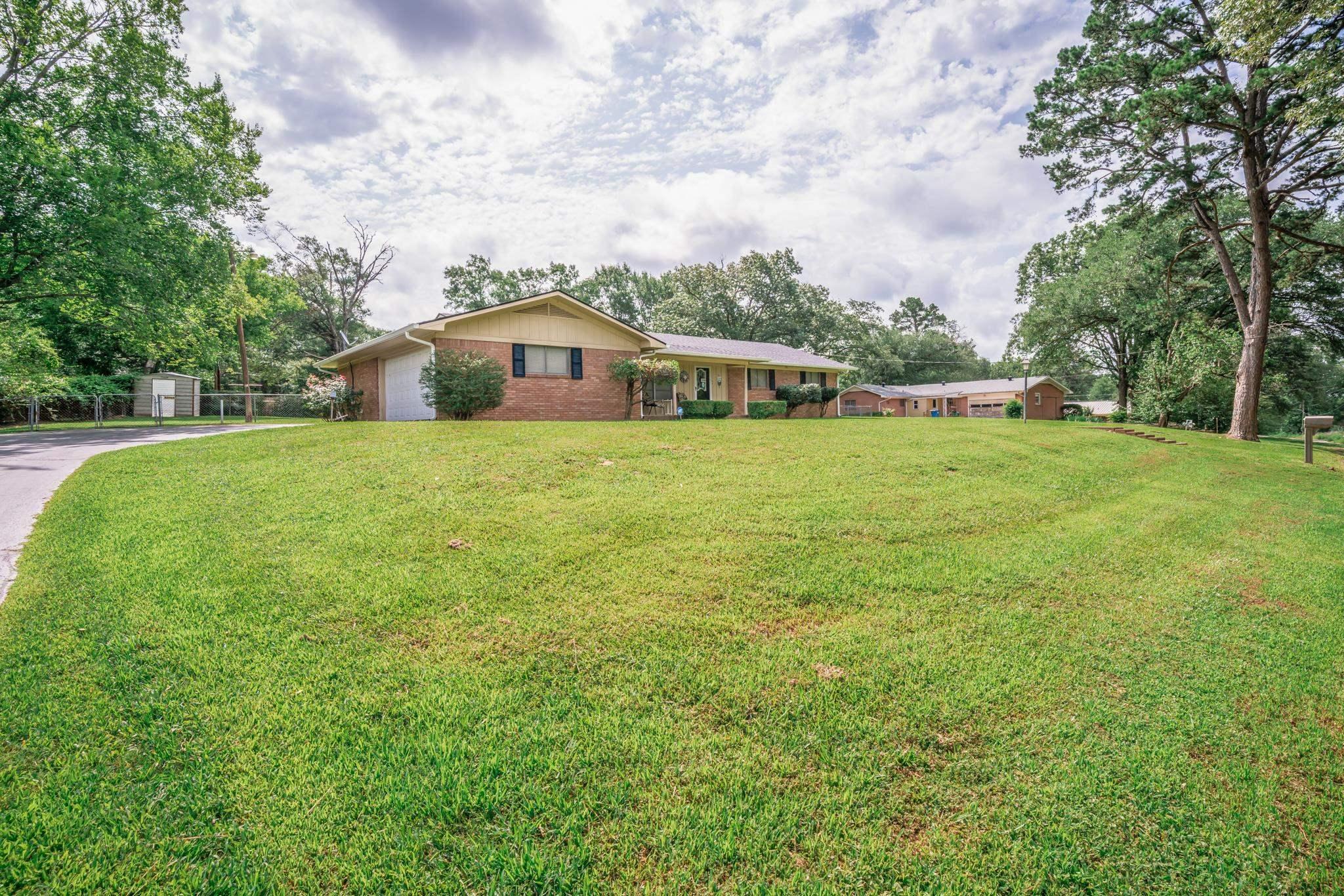 Image 1: Brick ranch-style residence featuring a prominent lawn, attached garage, and mature perimeter trees, Front Of Structure