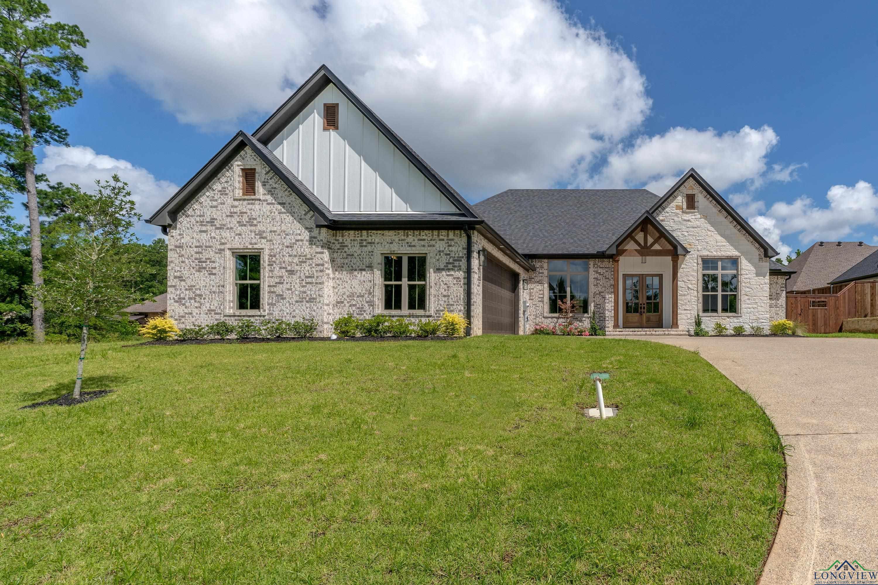 Image 2: View of front facade featuring board and batten siding, an attached garage, a front lawn, brick siding, and concrete driveway, Front Of Structure