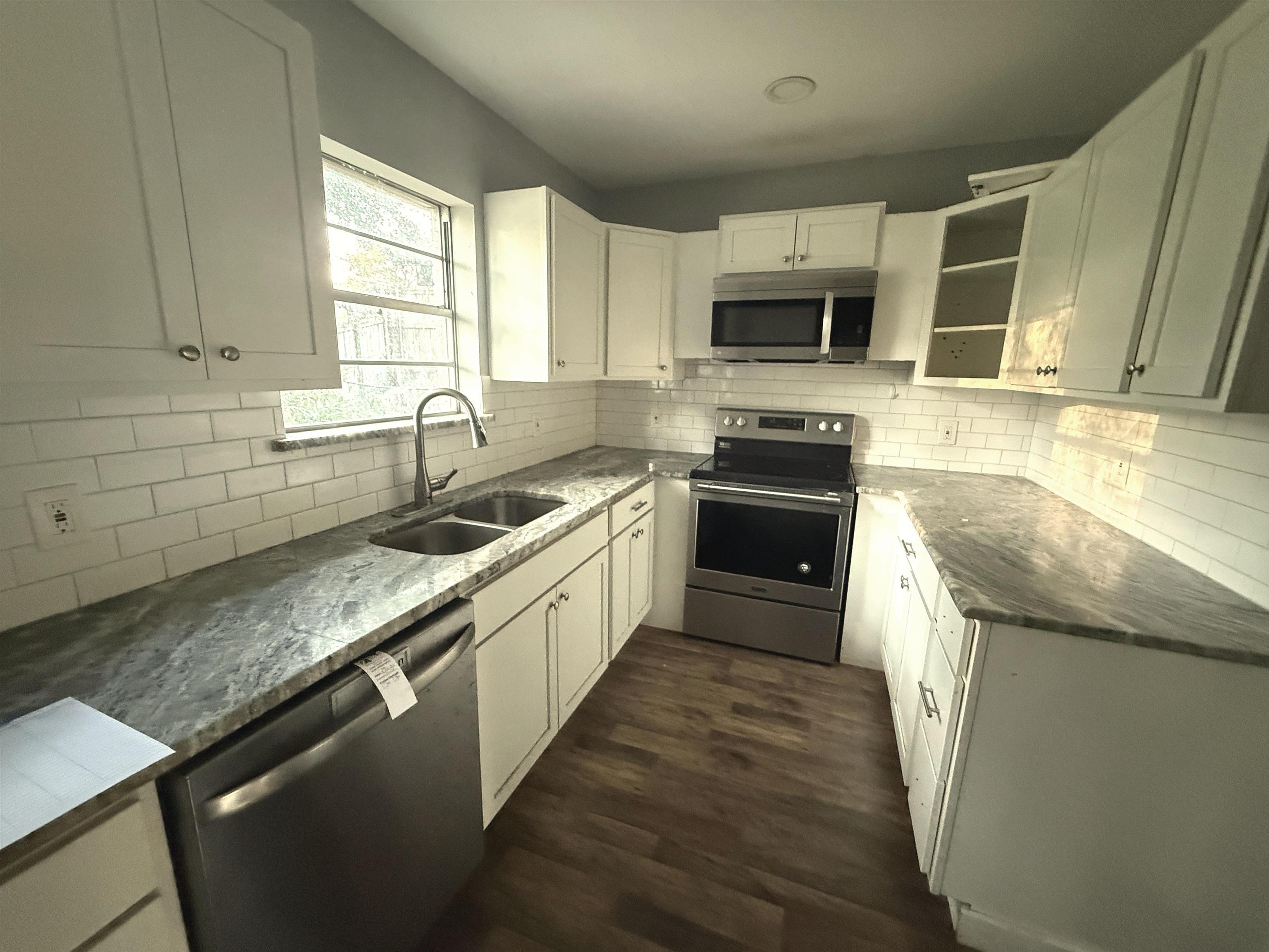 Image 3: Kitchen with stainless steel appliances, white cabinetry, dark stone countertops, dark wood finished floors, and tasteful backsplash, Kitchen