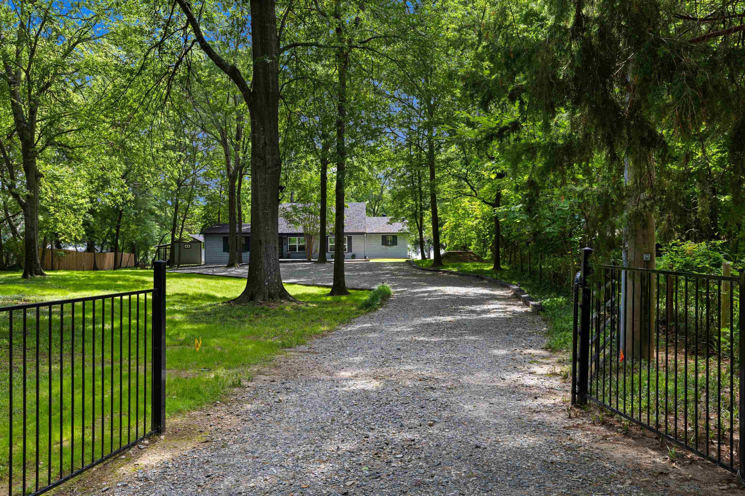Image 2: Gravel drive with a black metal gate and fencing, framed by mature trees, leading to a single-story residence, Front Of Structure