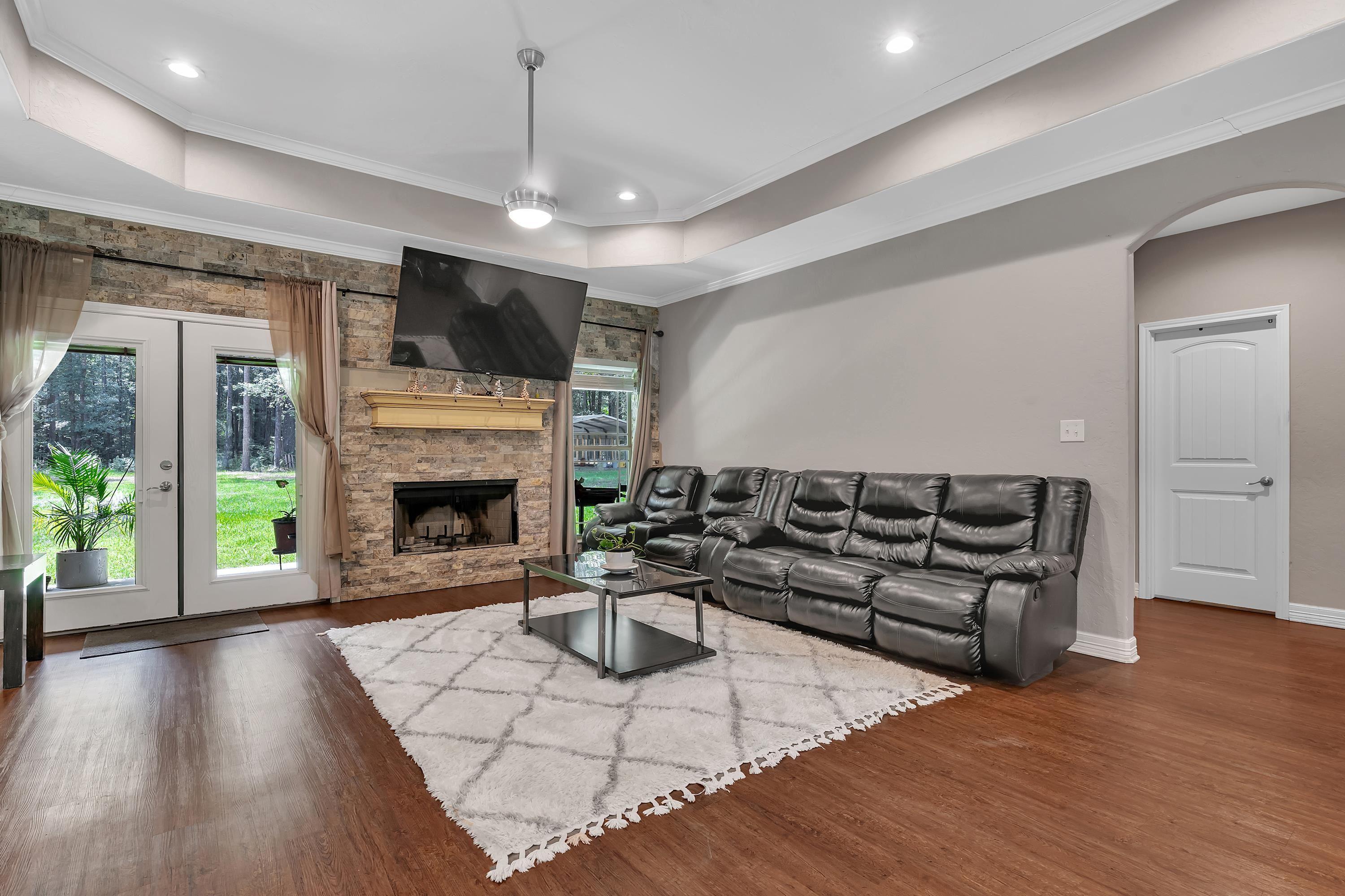 Image 3: Living room featuring a raised ceiling, crown molding, arched walkways, dark wood-style floors, and a stone fireplace, Living Room
